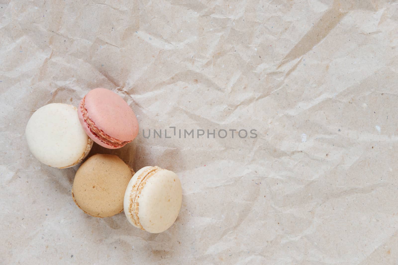 Pink, beige and brown almond cookies (macaroons) on the background of crumpled craft paper; top view