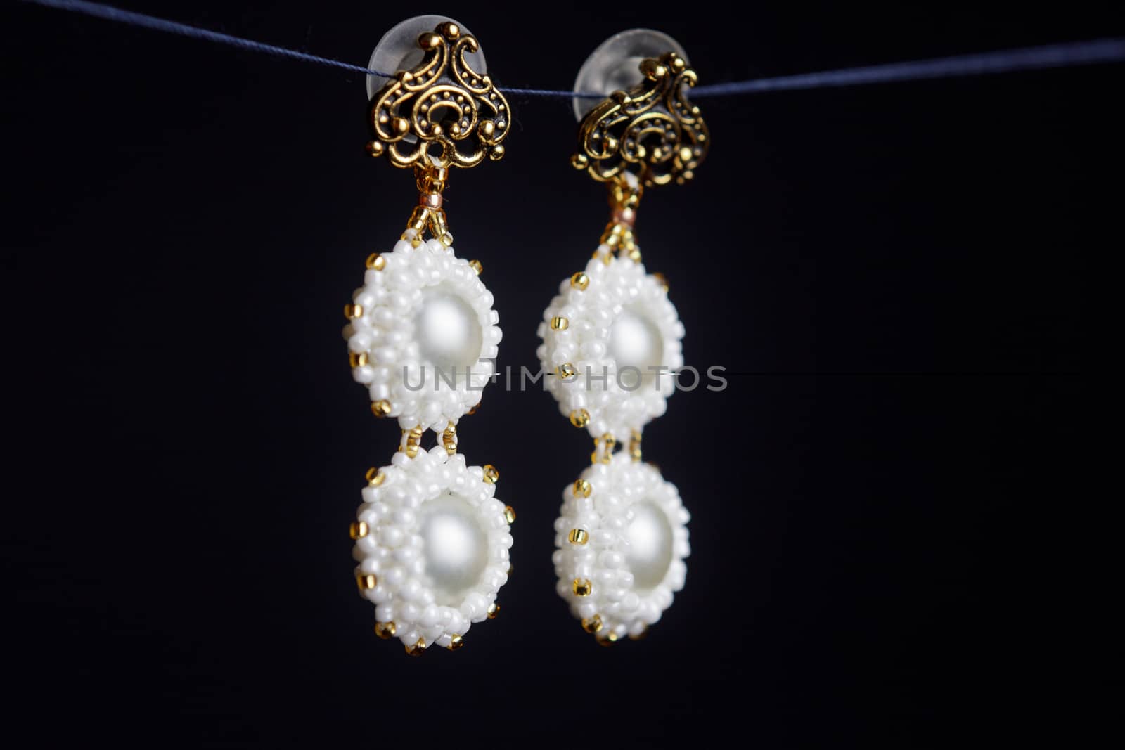 handmade jewelry made of beads in macro. earrings from white beads. earrings from stones. beautiful ornaments. earrings from white beads. ornaments on a black background by yulaphotographer