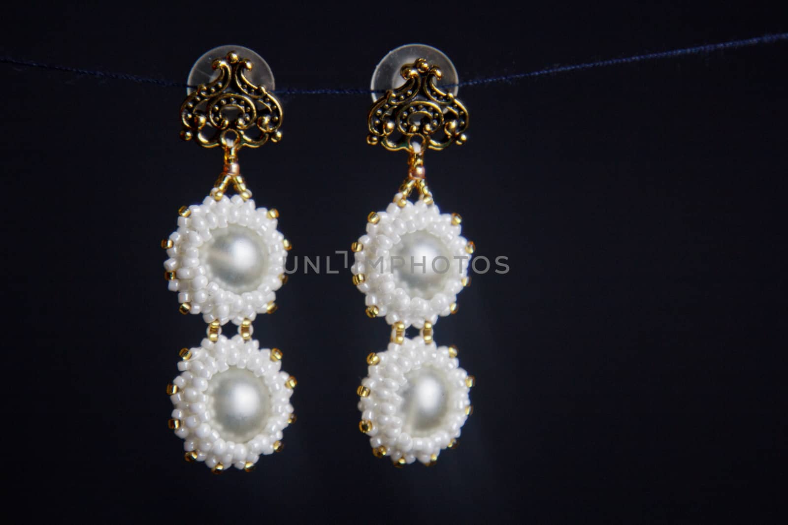 handmade jewelry made of beads in macro. earrings from white beads. earrings from stones. beautiful ornaments. earrings from white beads. ornaments on a black background by yulaphotographer