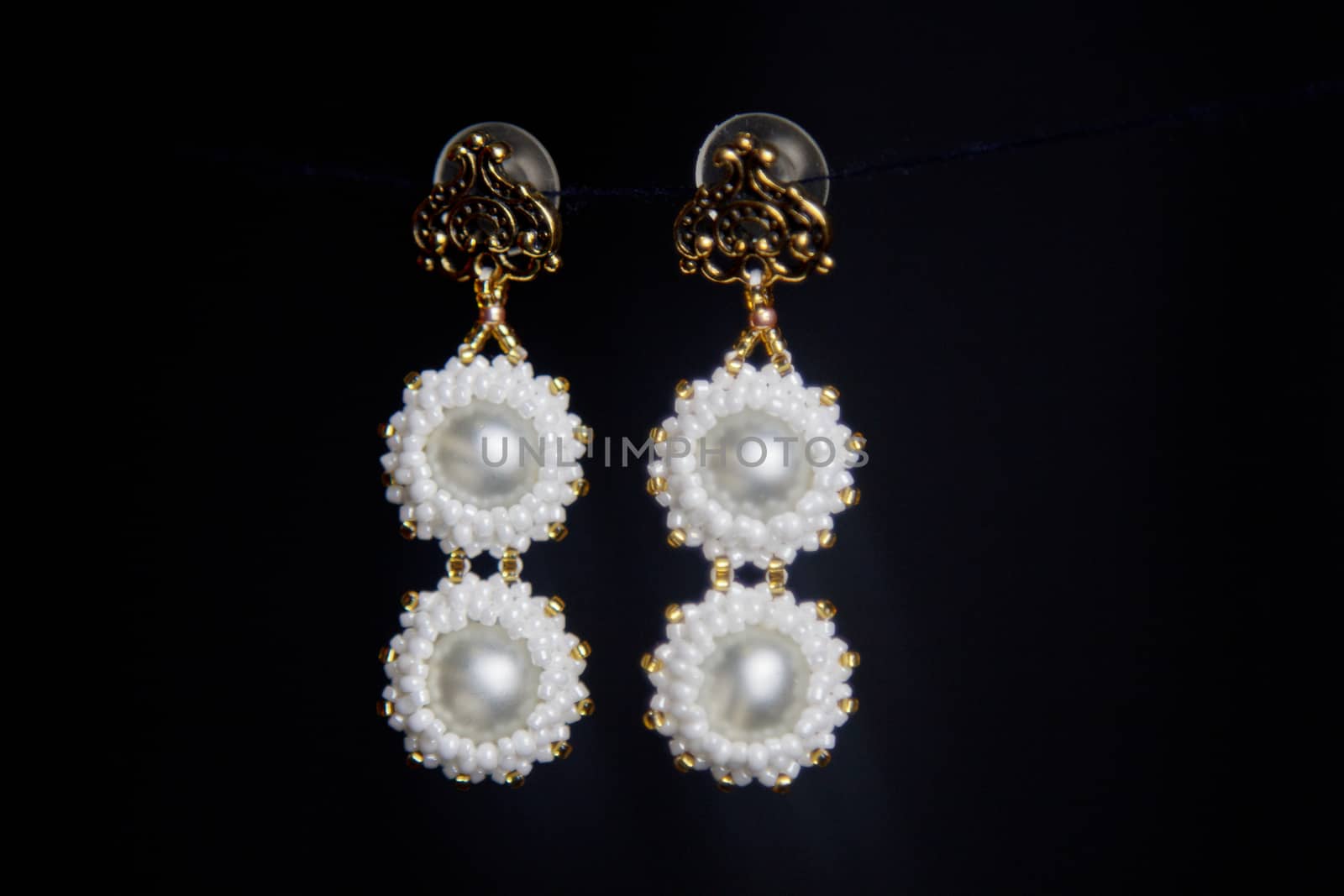 handmade jewelry made of beads in macro. earrings from white beads. earrings from stones. beautiful ornaments. earrings from white beads. ornaments on a black background by yulaphotographer