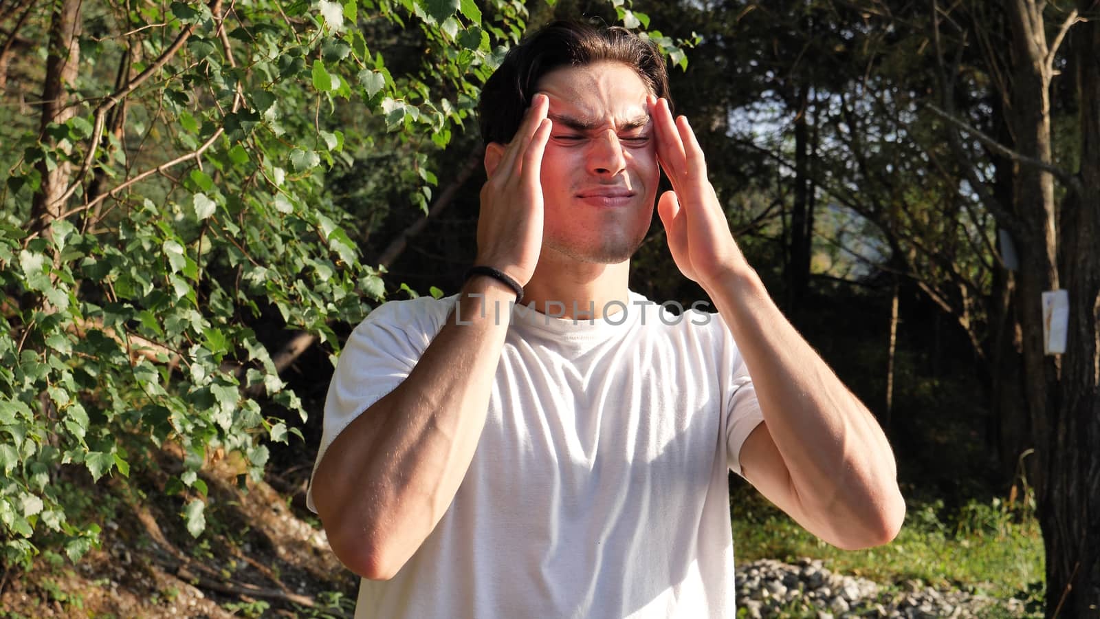 Young handsome man standing in nature, in pain, suffering from headache or migraine