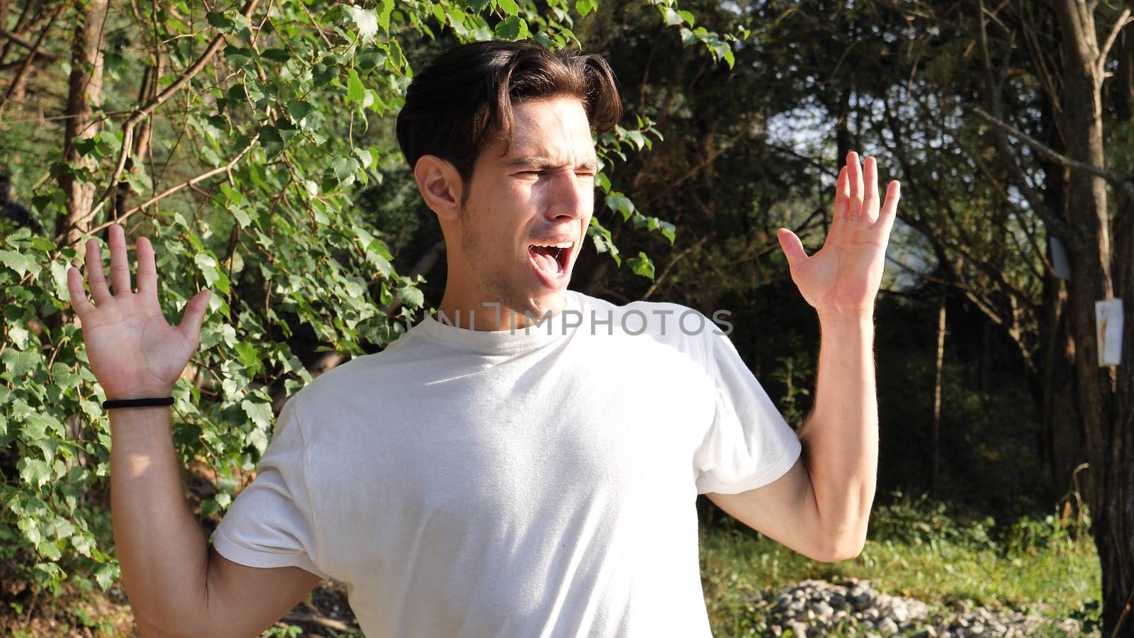 Young handsome man standing in nature, covering ears in pain and frustration because of too much loud noise