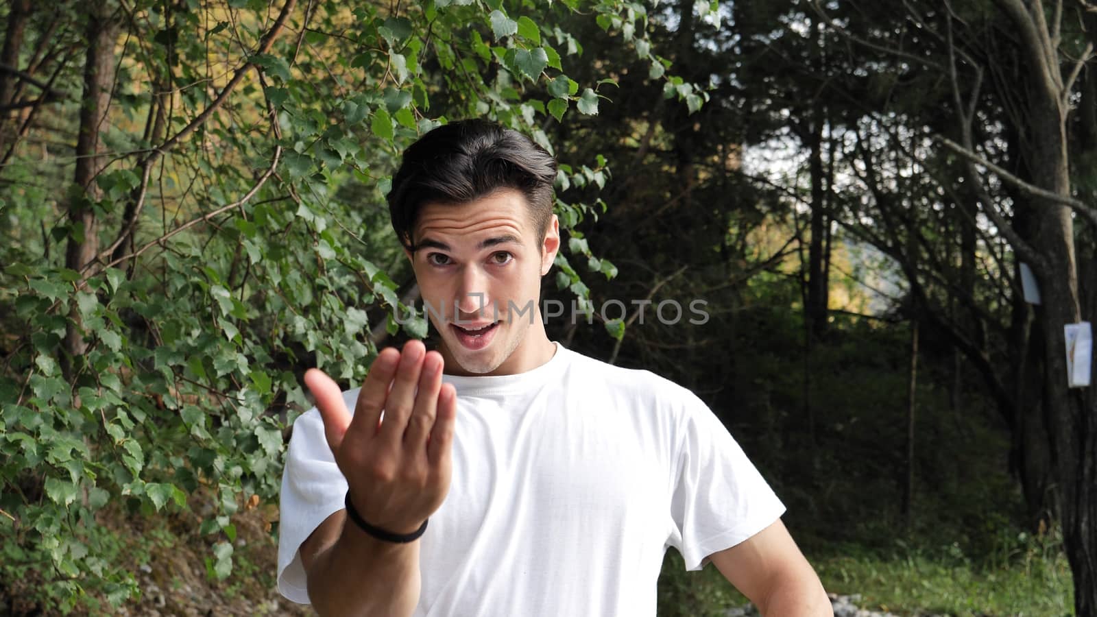 Young handsome man standing in nature, saying Come Here or Come Closer with hand gesturing