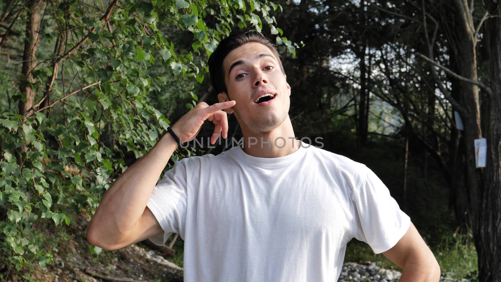 Young handsome man standing in nature, doing Call Me sign with hand, gesturing like he has a telephone