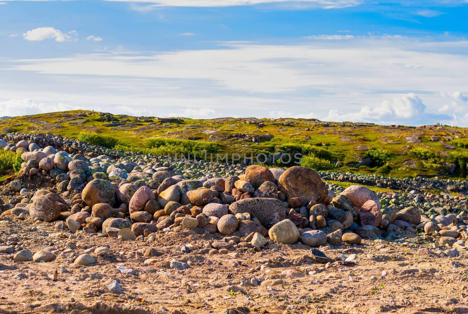 A handful of huge stones surrounded by grass. Bright sky in the clouds. Hills in the background.
