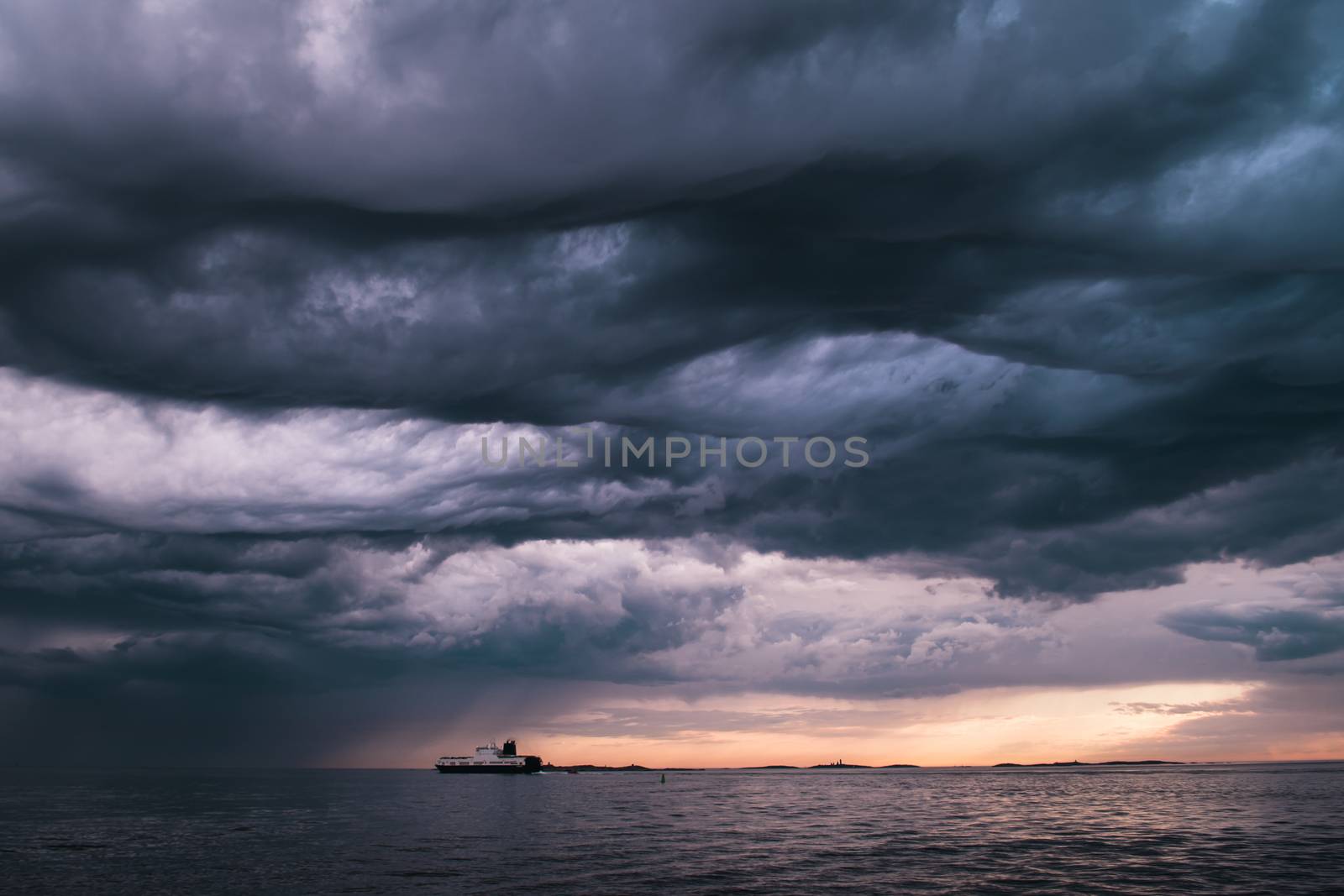 A cargo ship underneath stormy clouds during sunset