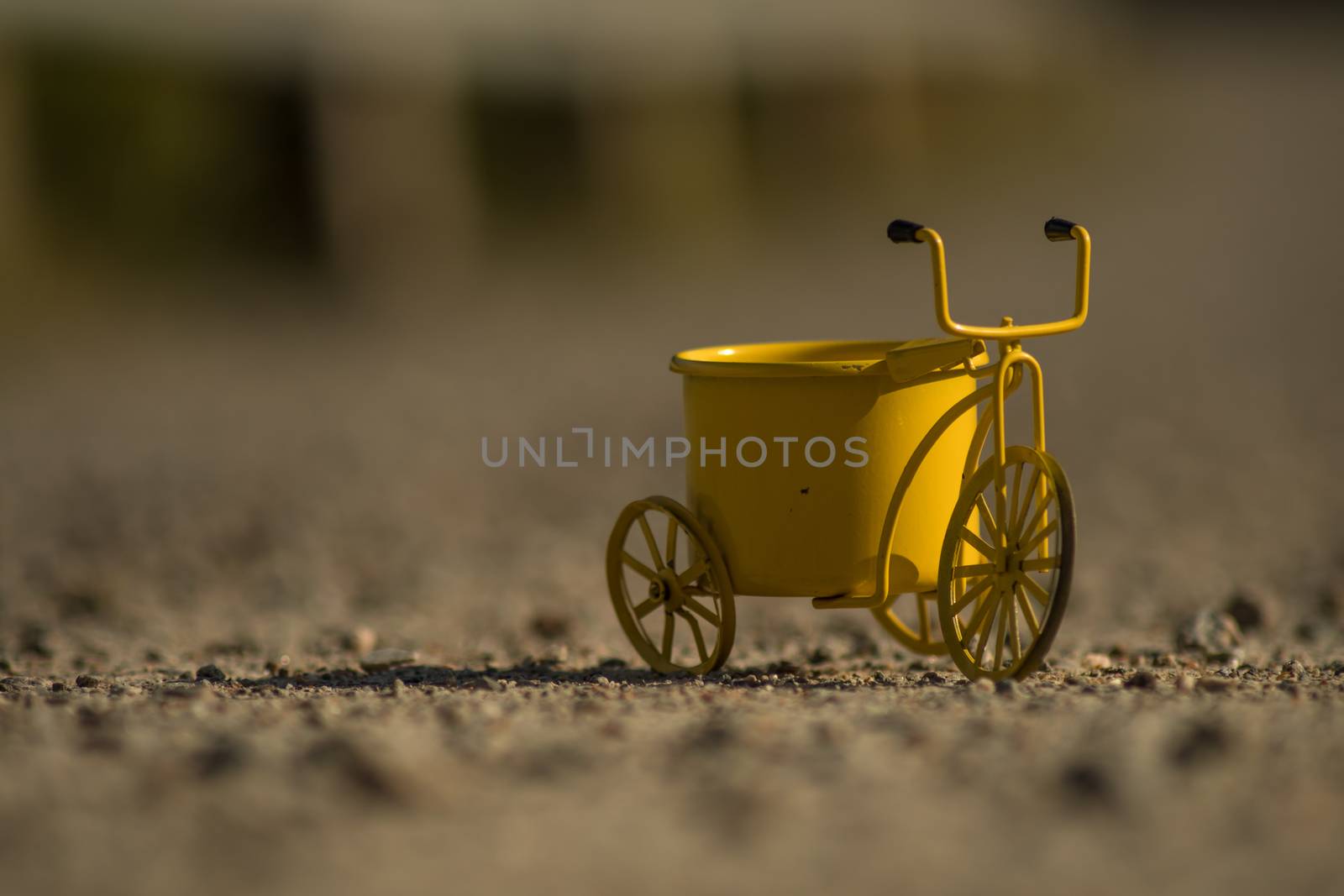 A yellow toy tricycle on a gravel road