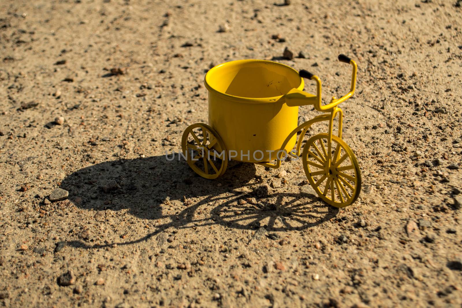 A yellow toy tricycle on a gravel road