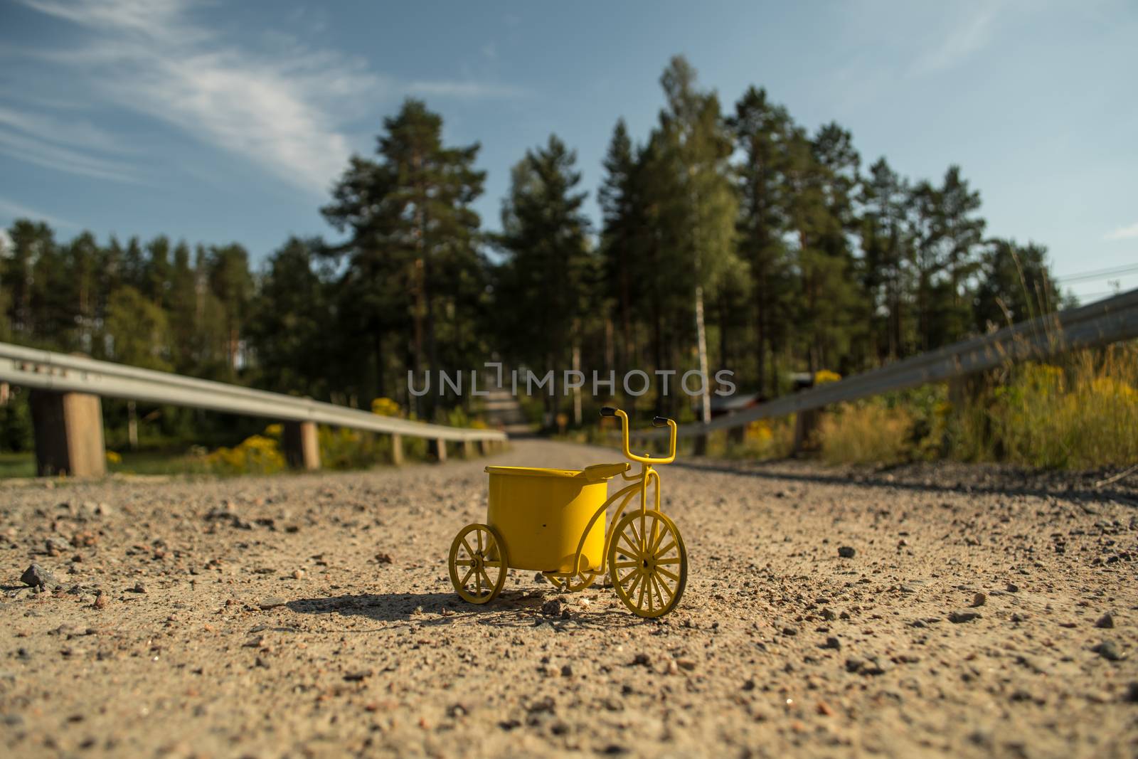 A yellow toy tricycle on a gravel road