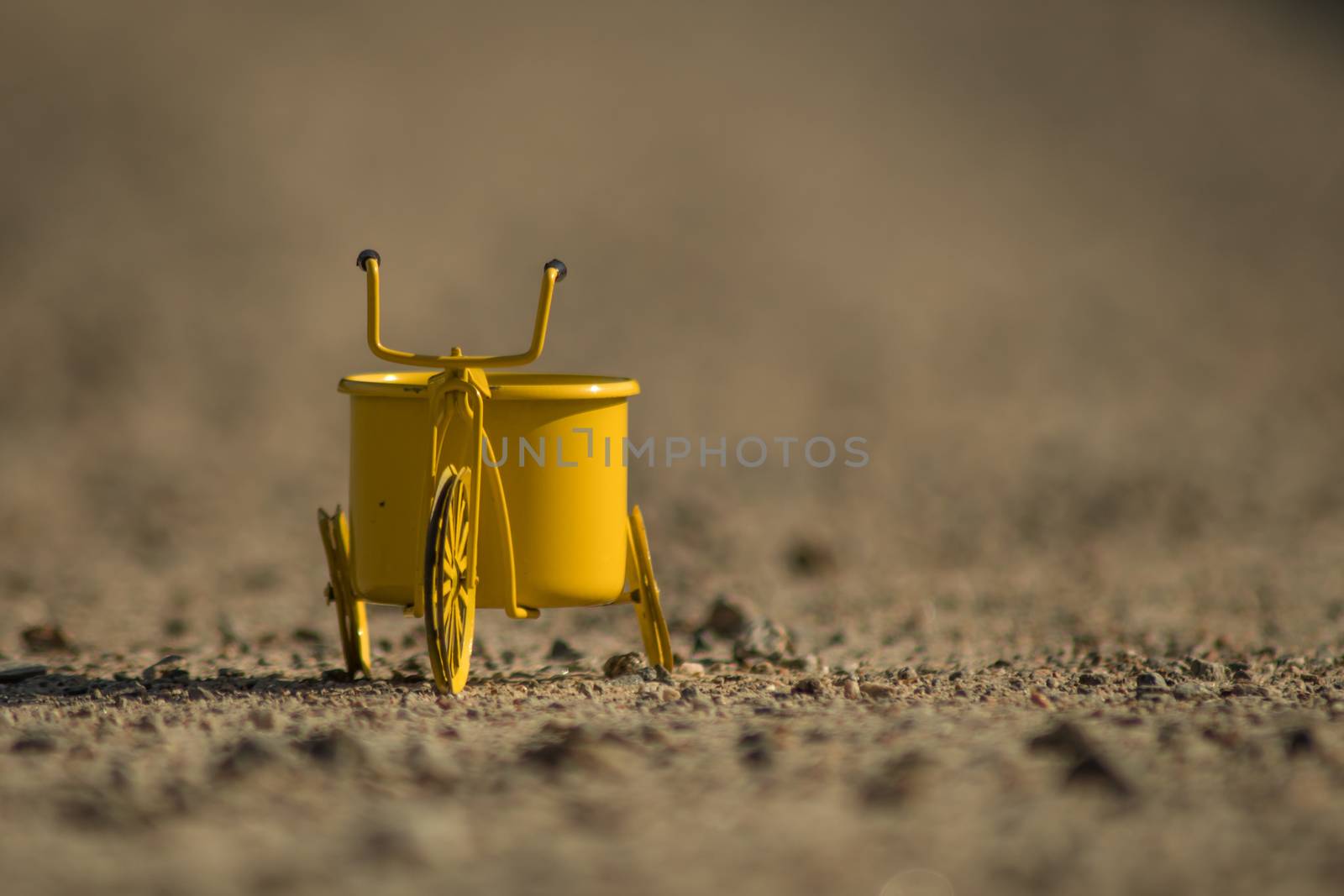 A yellow toy tricycle on a gravel road