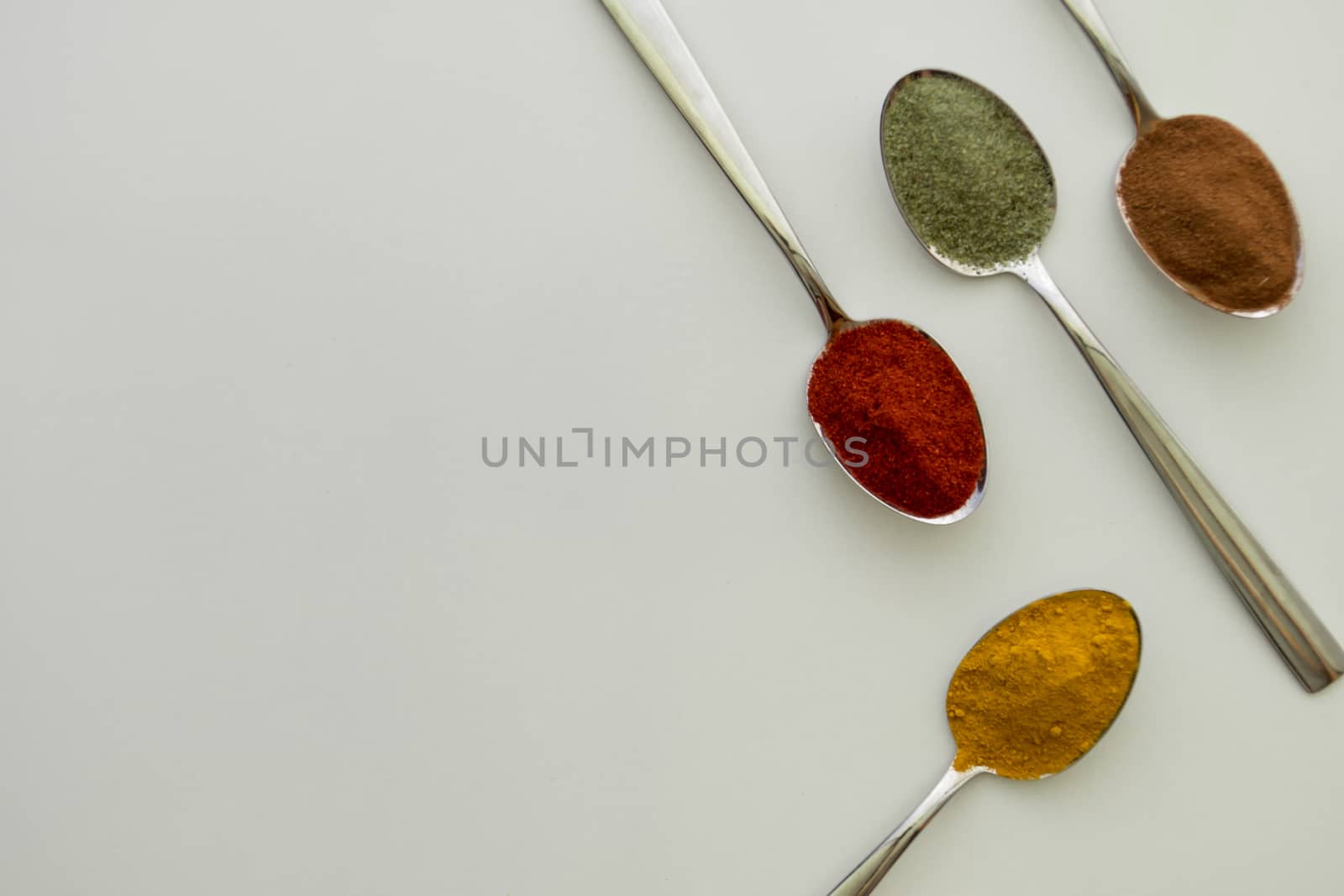 Various colorful spices arranged on spoons  with a white background