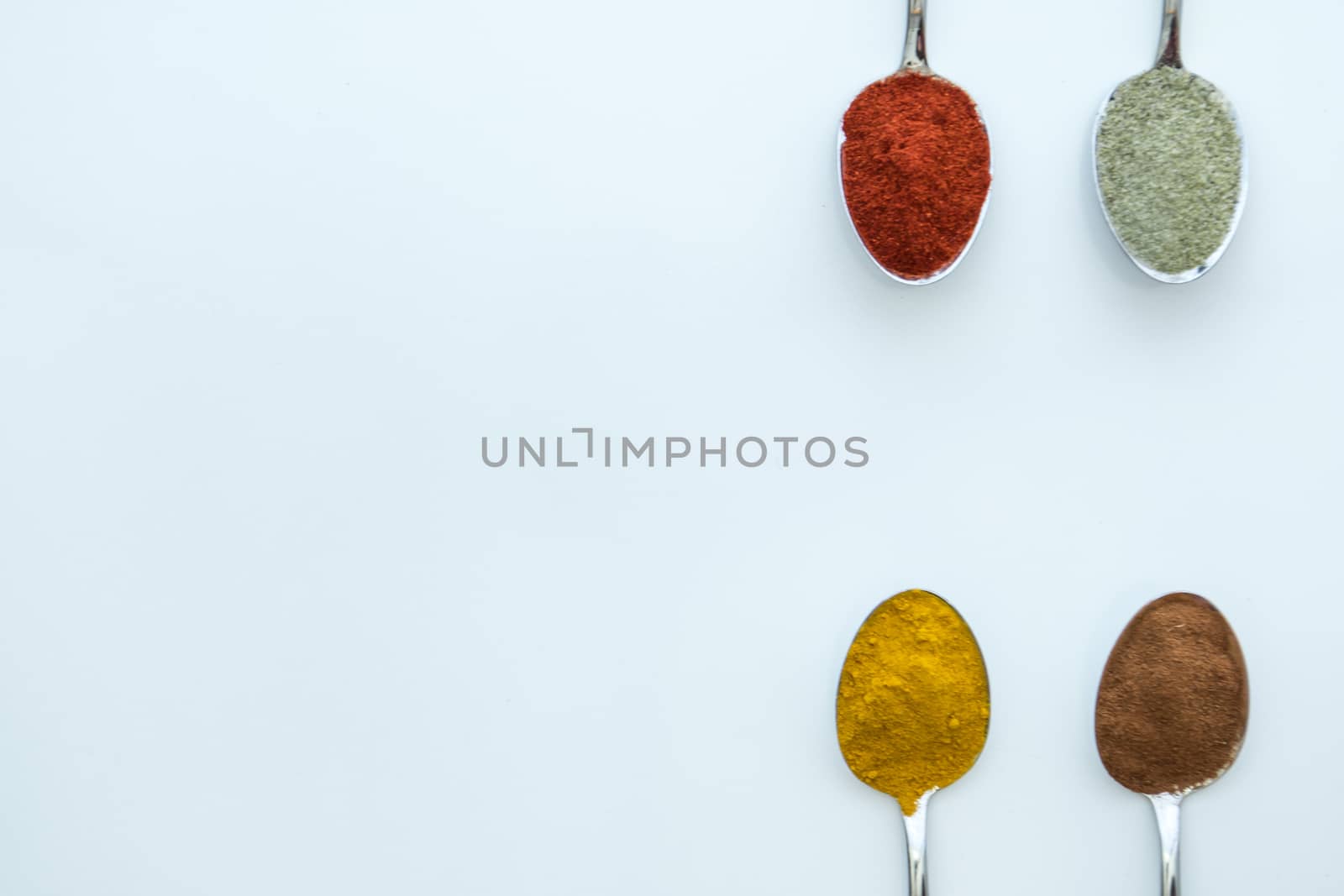 Various colorful spices arranged on spoons  with a white background