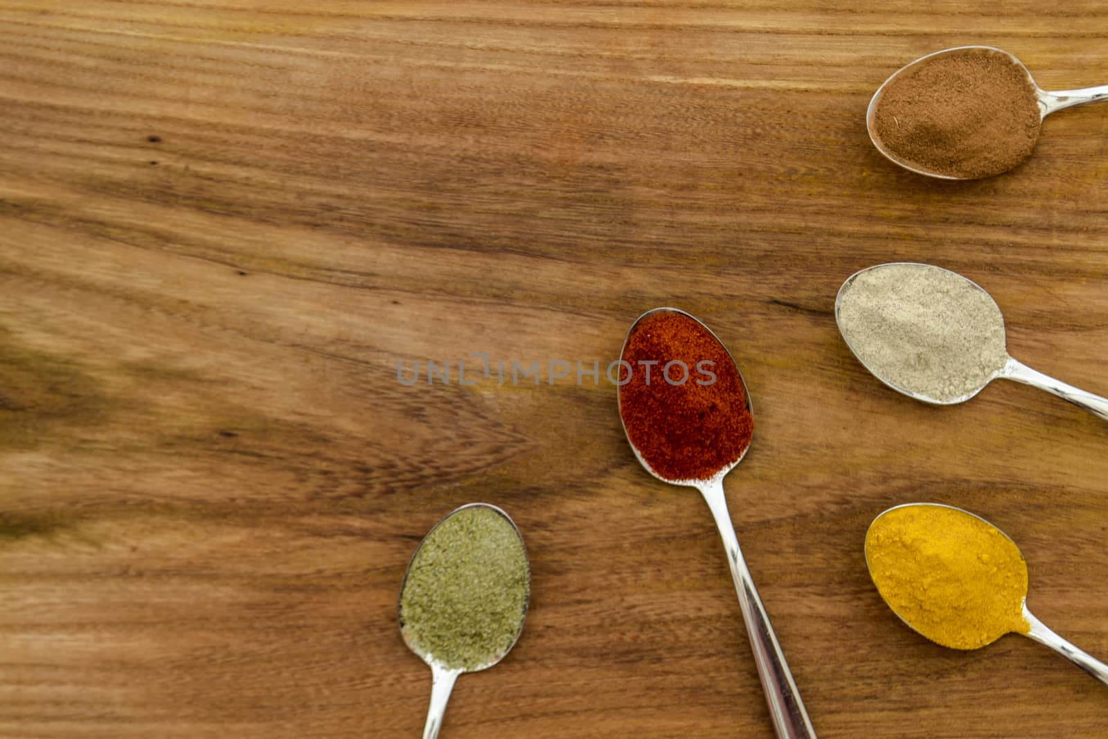 Various colorful spices arranged on spoons  with wooden background