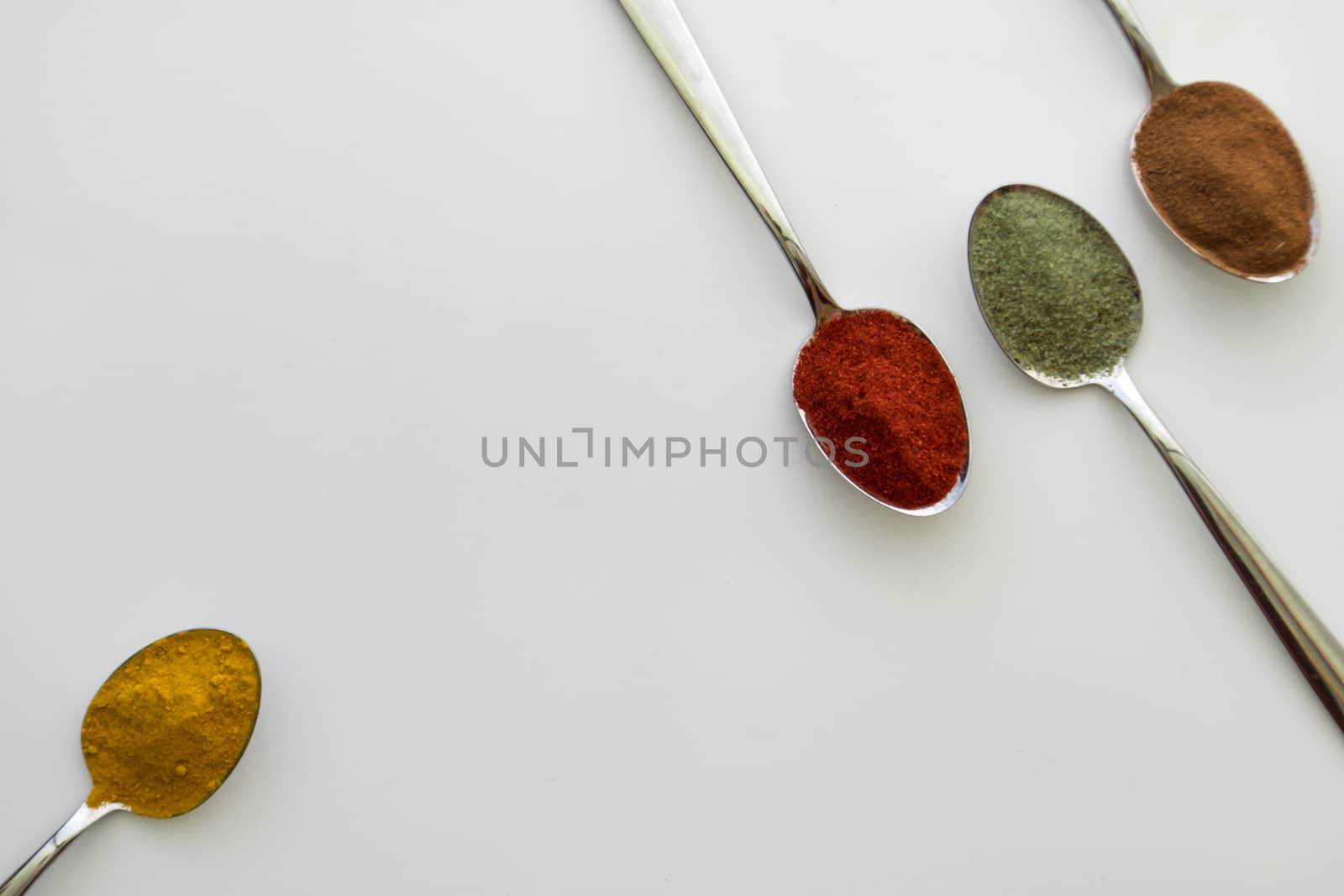 Various colorful spices arranged on spoons  with a white background