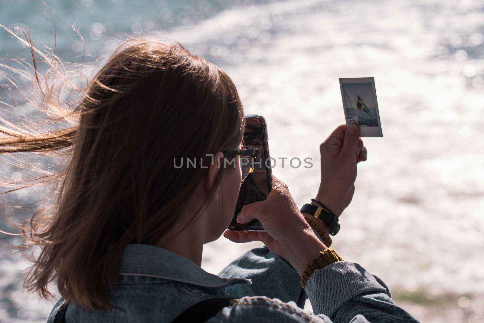 A young girl photographing a polaroid photo with her phone