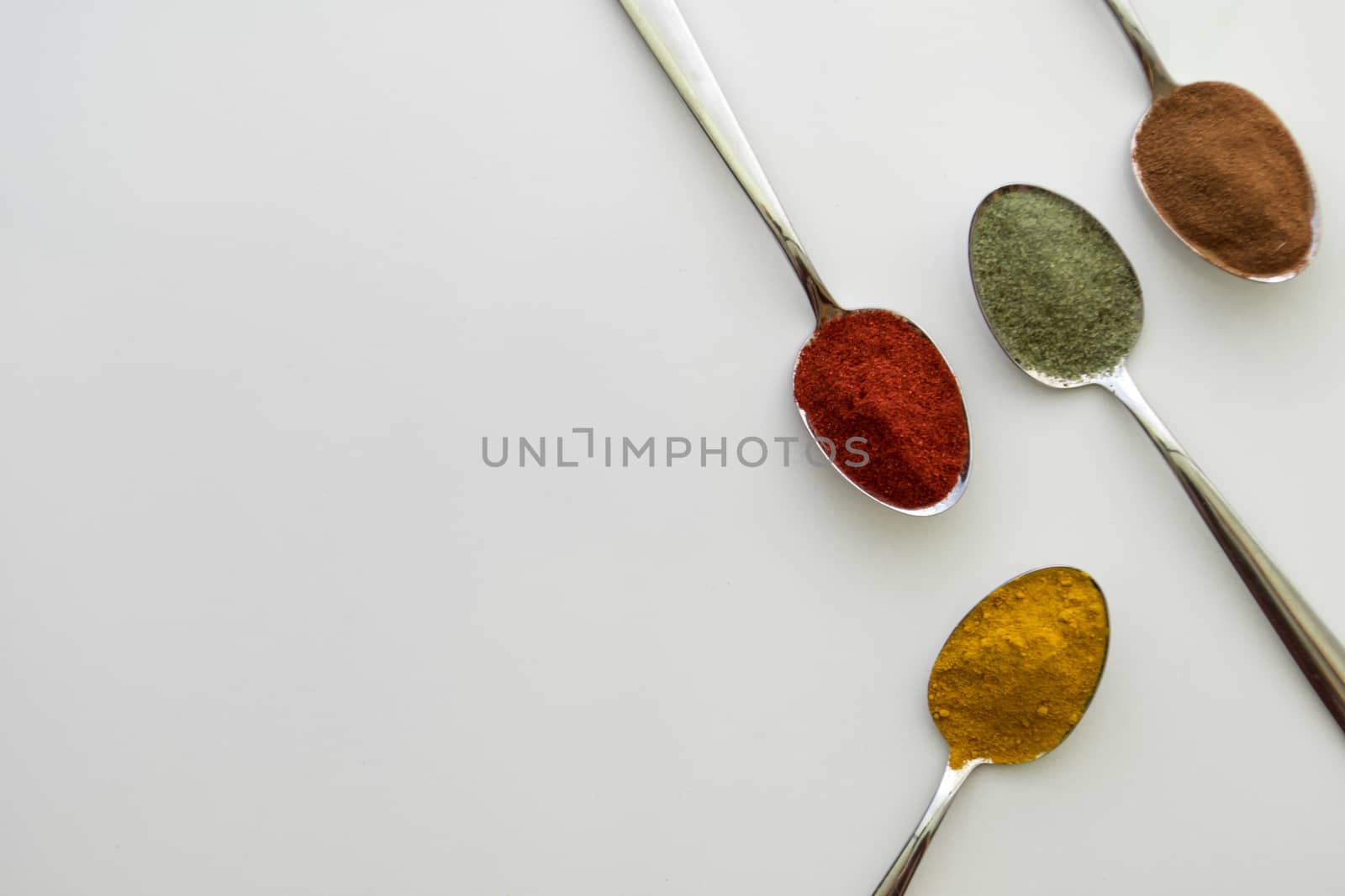 Various colorful spices arranged on spoons  with a white background