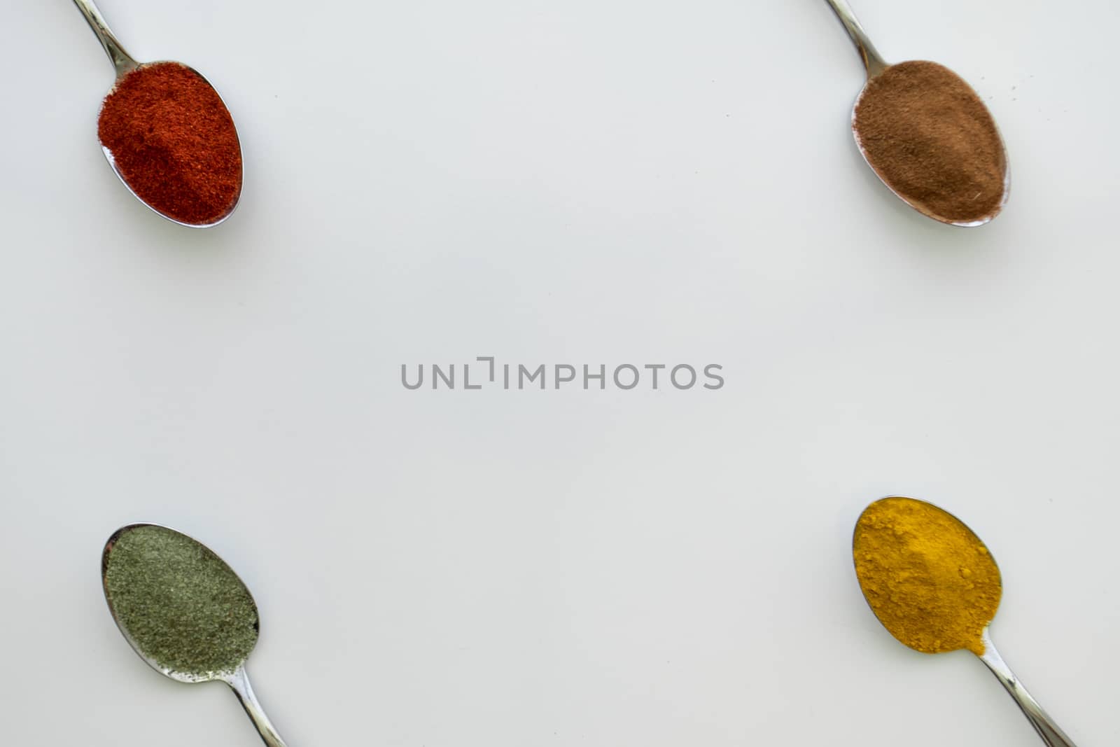 Various colorful spices arranged on spoons  with a white background