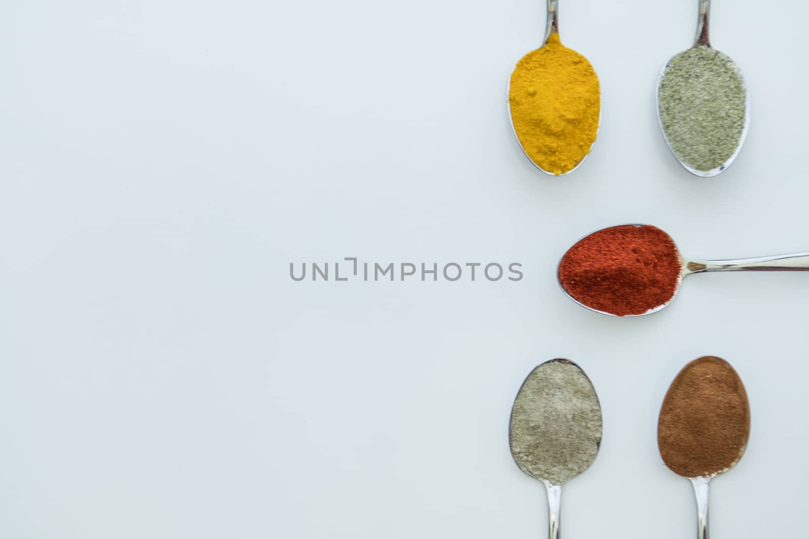 Various colorful spices arranged on spoons  with a white background