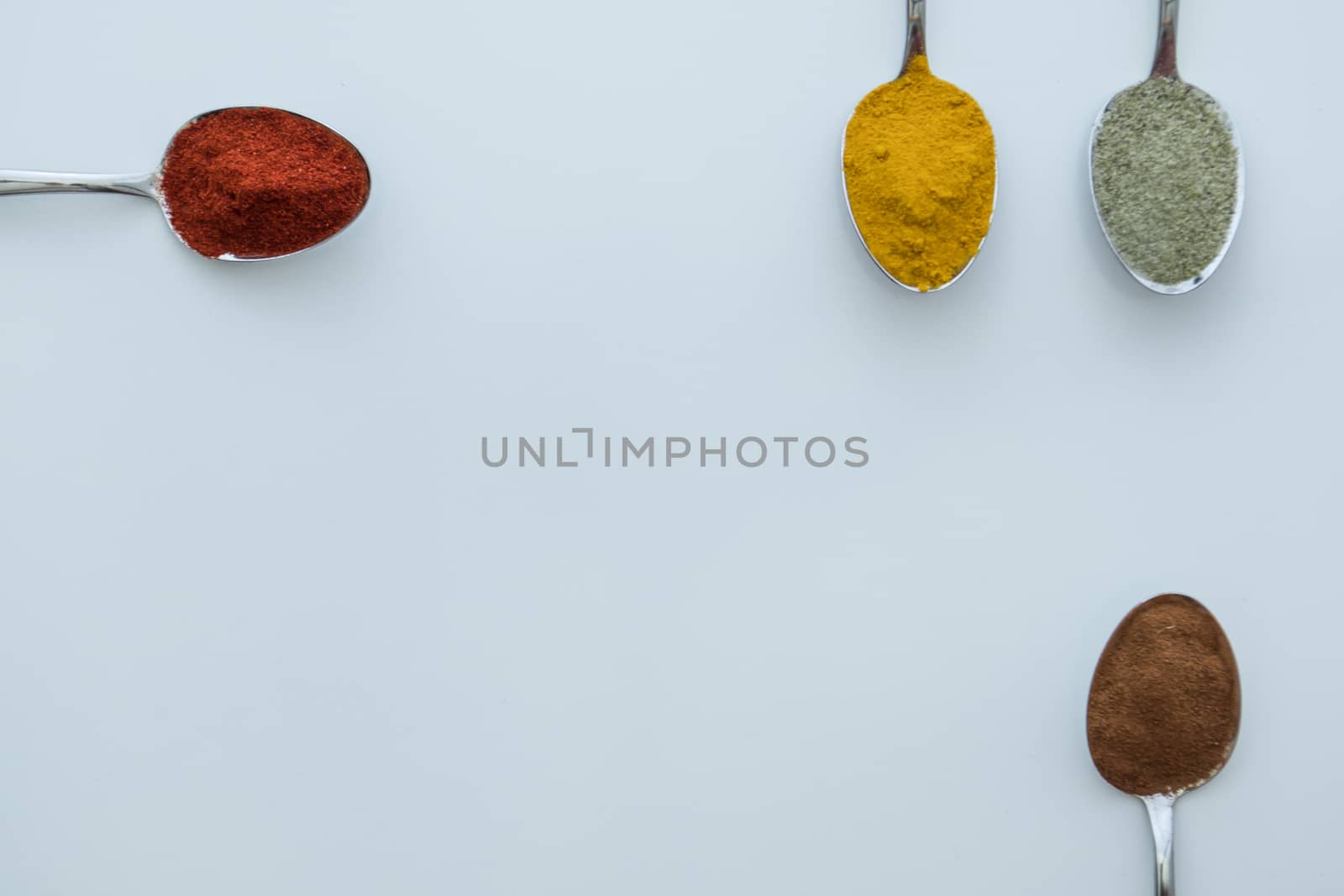 Various colorful spices arranged on spoons  with a white background