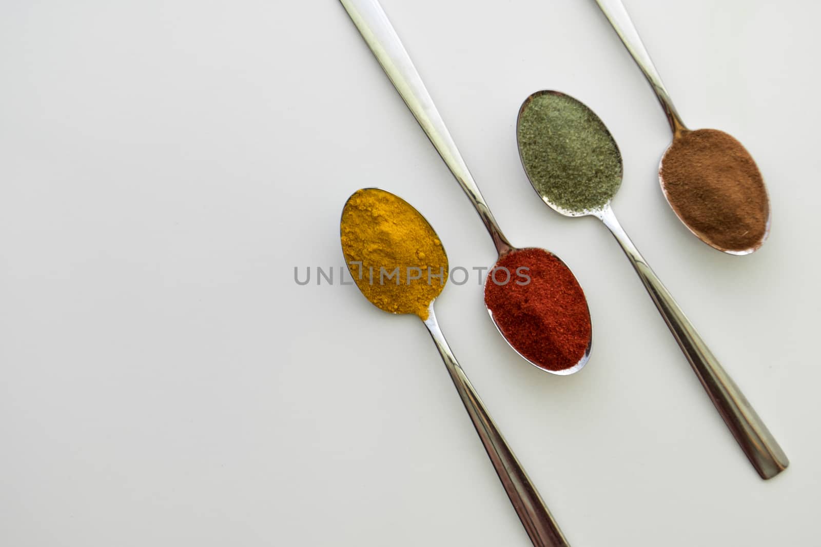 Various colorful spices arranged on spoons  with a white background