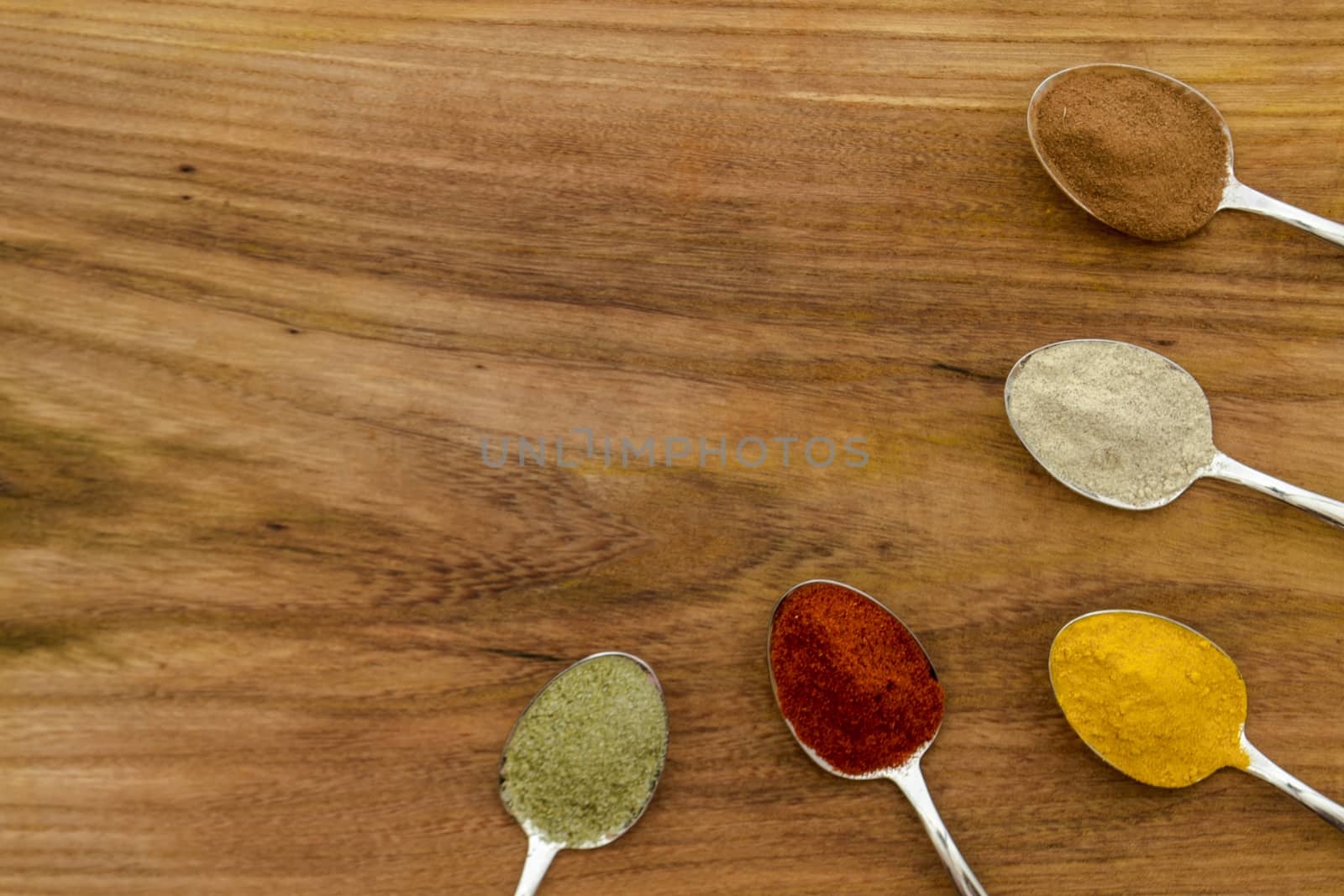 Various colorful spices arranged on spoons  with wooden background