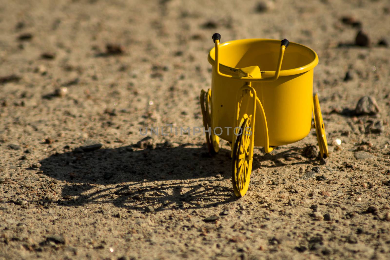 A yellow toy tricycle on a gravel road