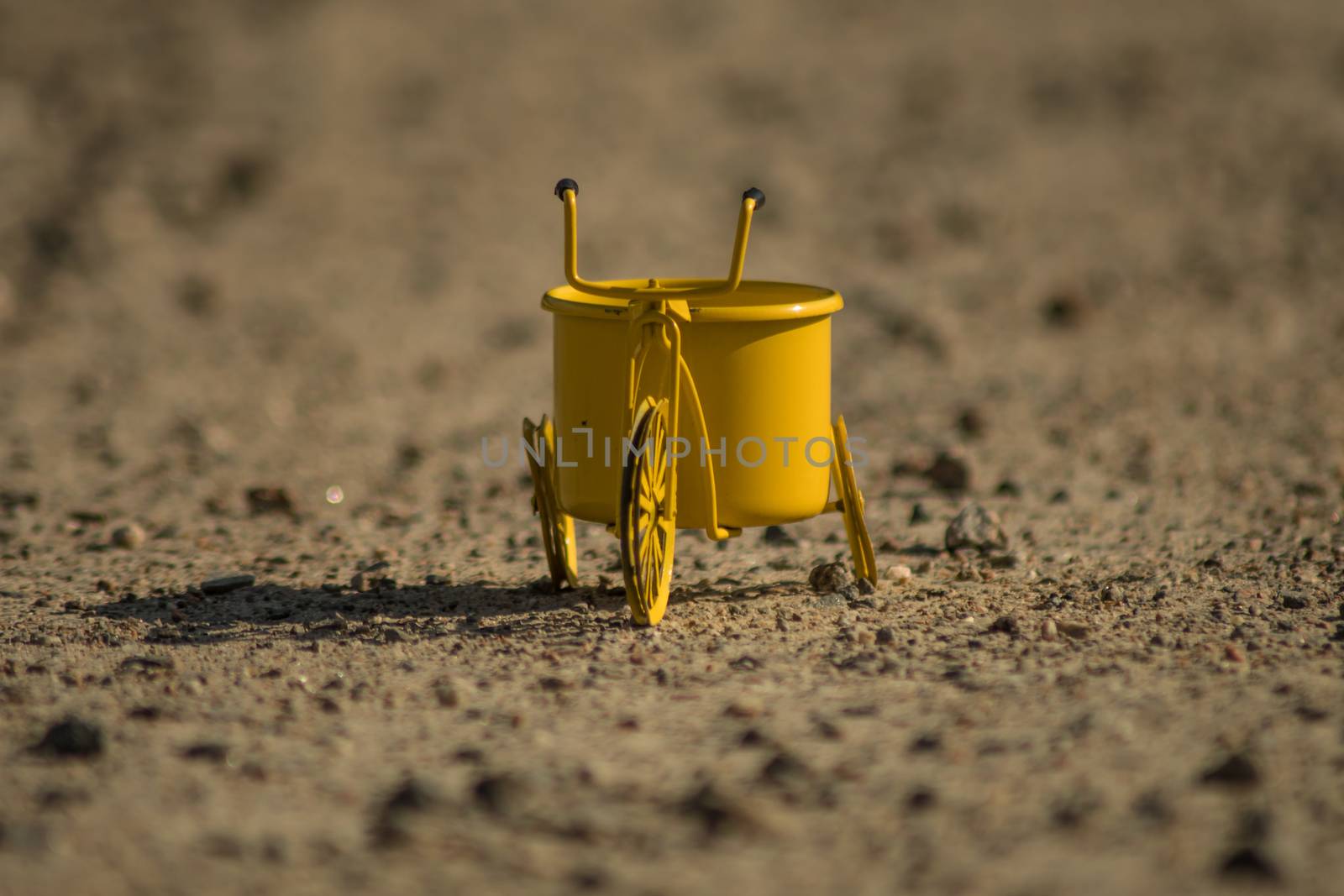 A yellow toy tricycle on a gravel road