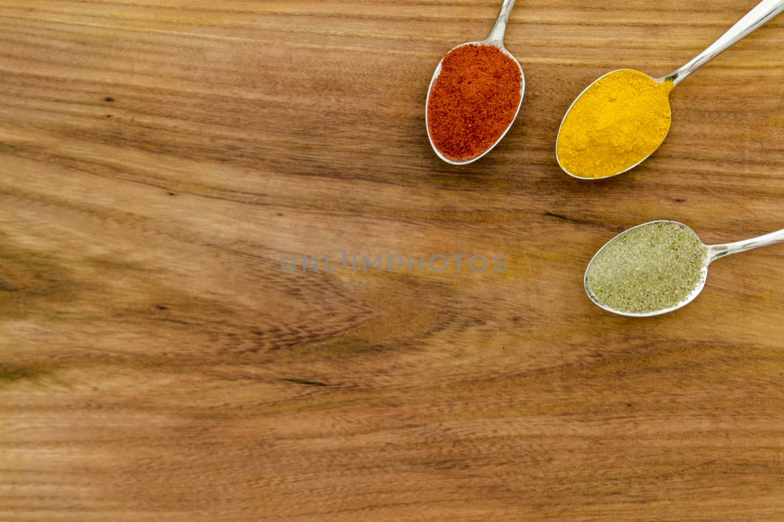 Various colorful spices arranged on spoons  with wooden background