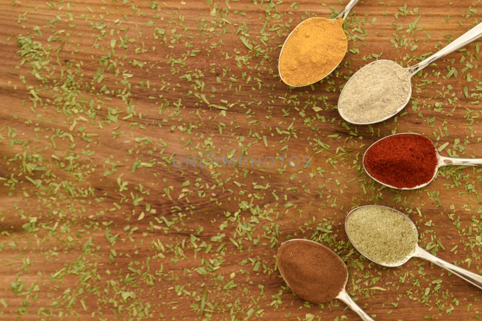 Various colorful spices arranged on spoons  with wooden background