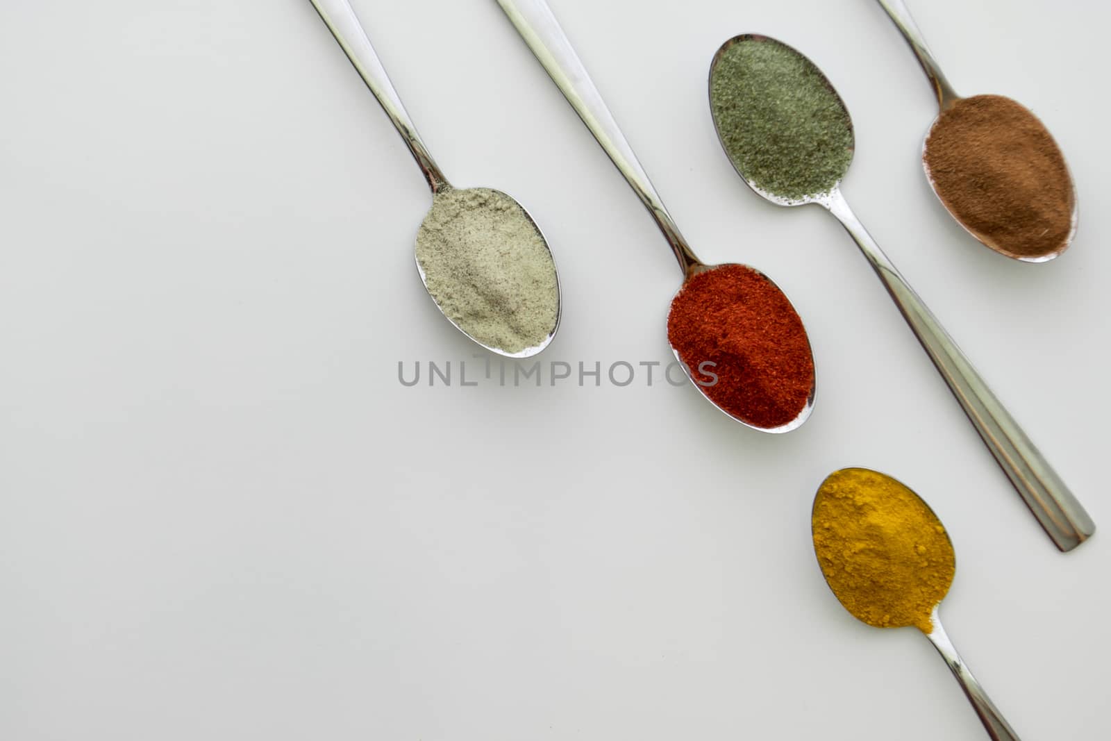 Various colorful spices arranged on spoons  with a white background