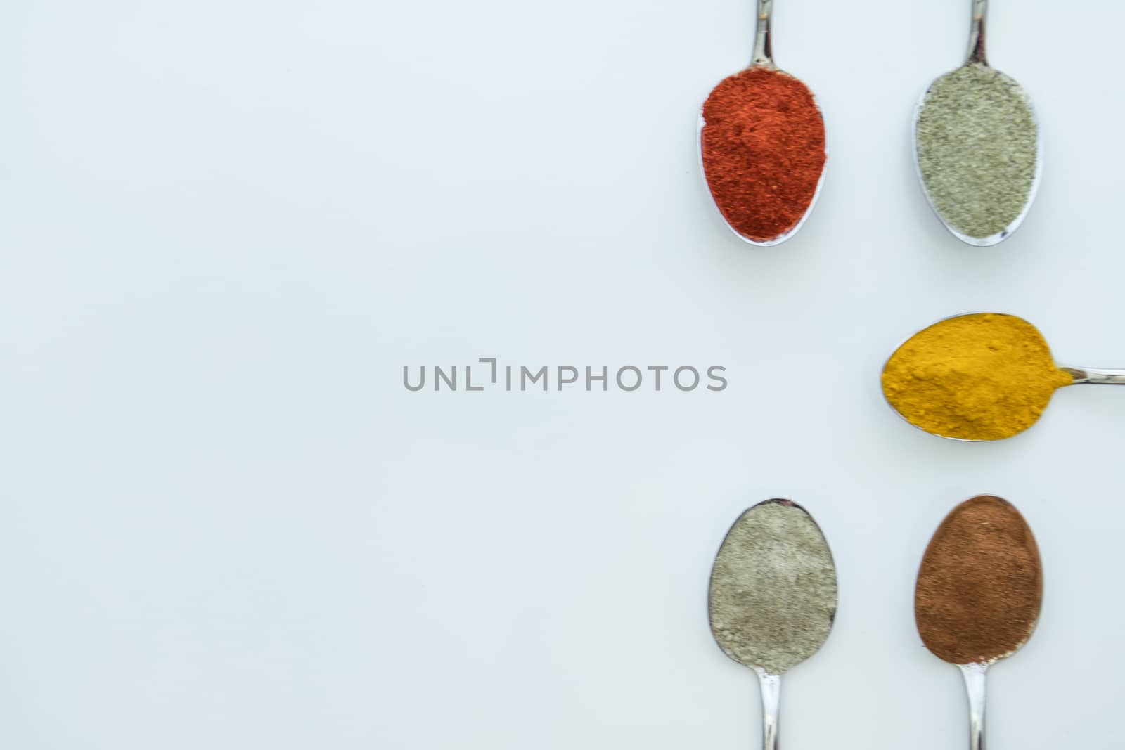 Various colorful spices arranged on spoons  with a white background