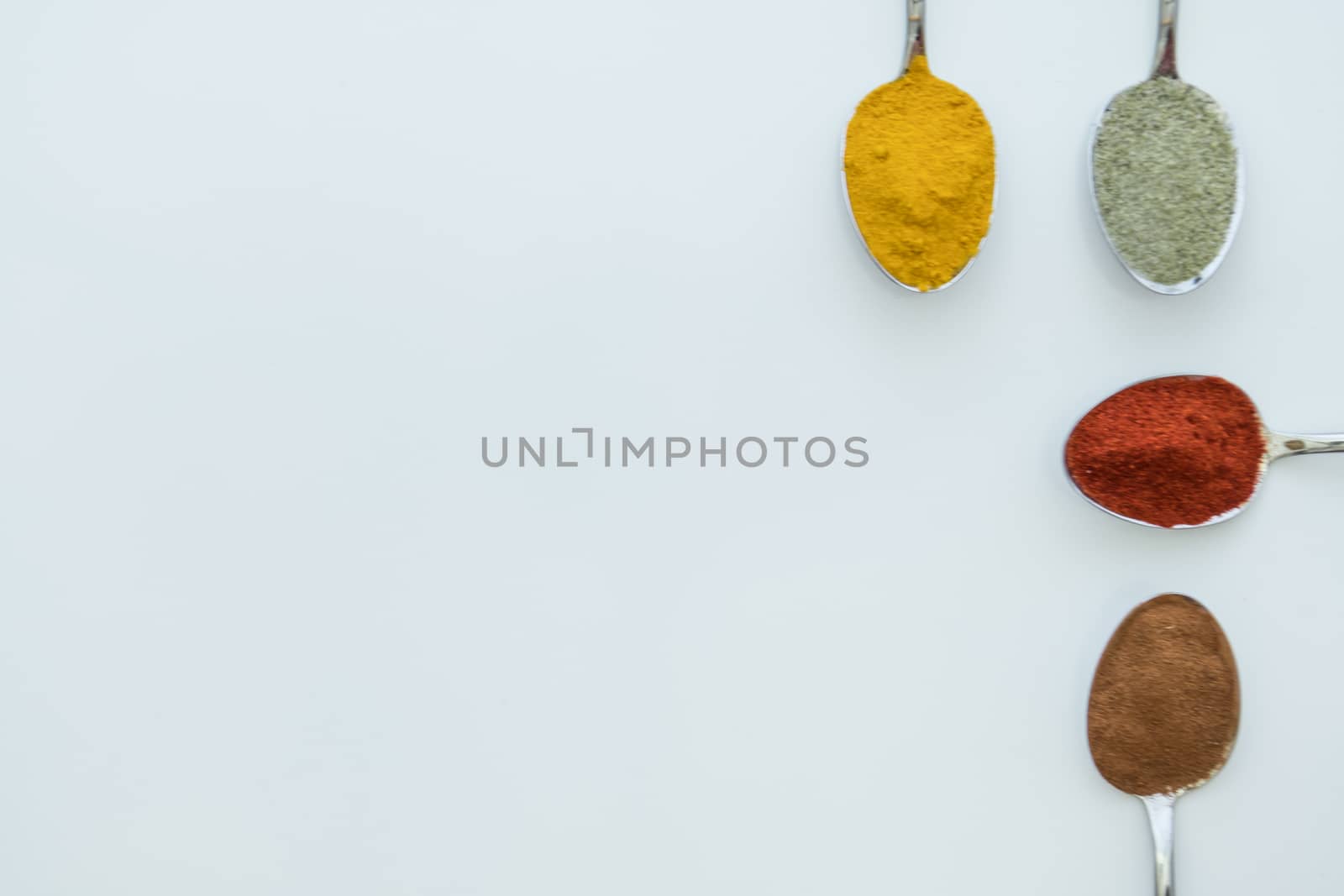 Various colorful spices arranged on spoons  with a white background