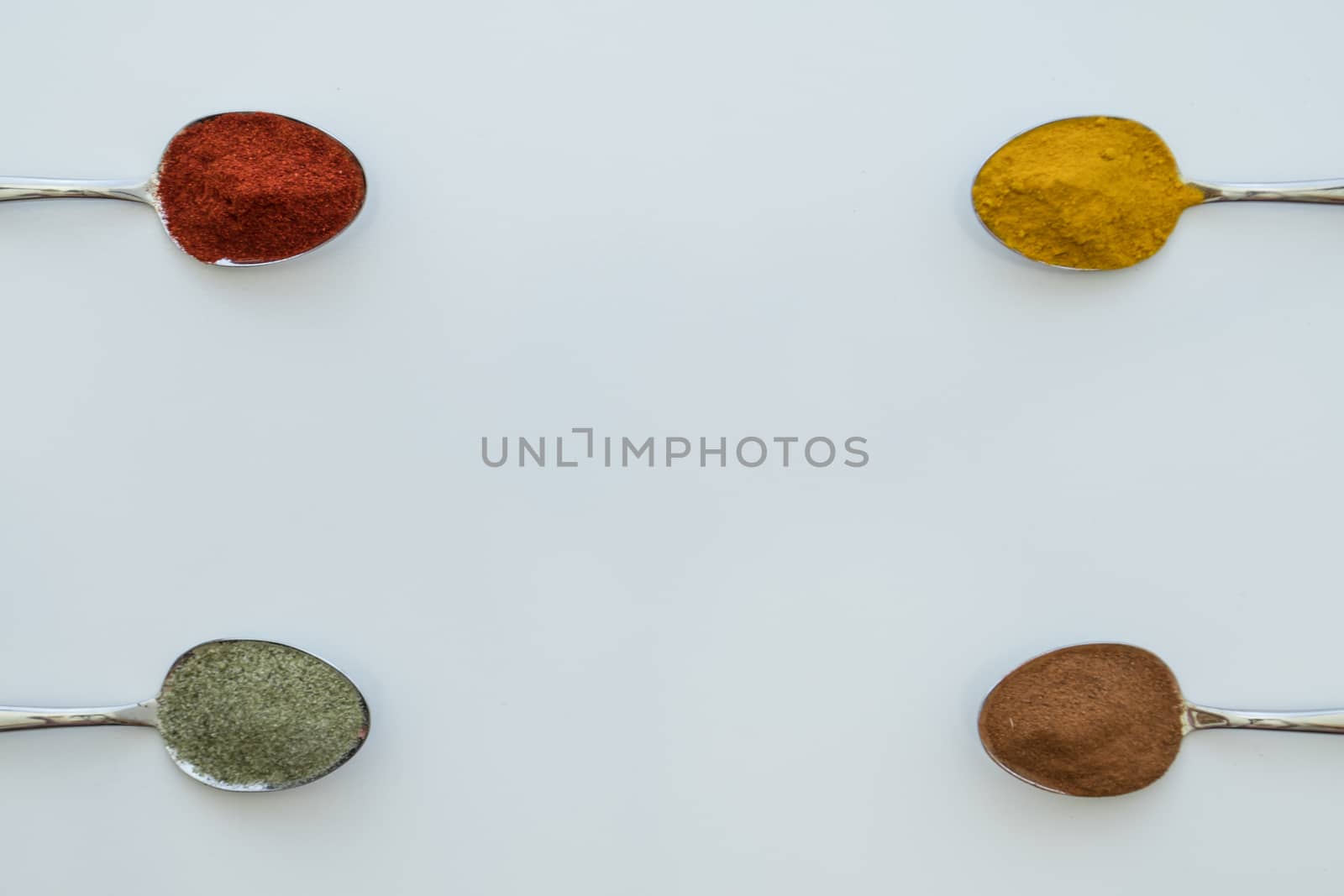 Various colorful spices arranged on spoons  with a white background