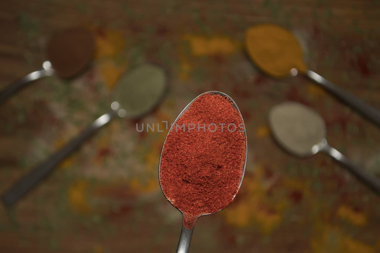 Closeup of red paprika spice on a spoon with other spices in the background