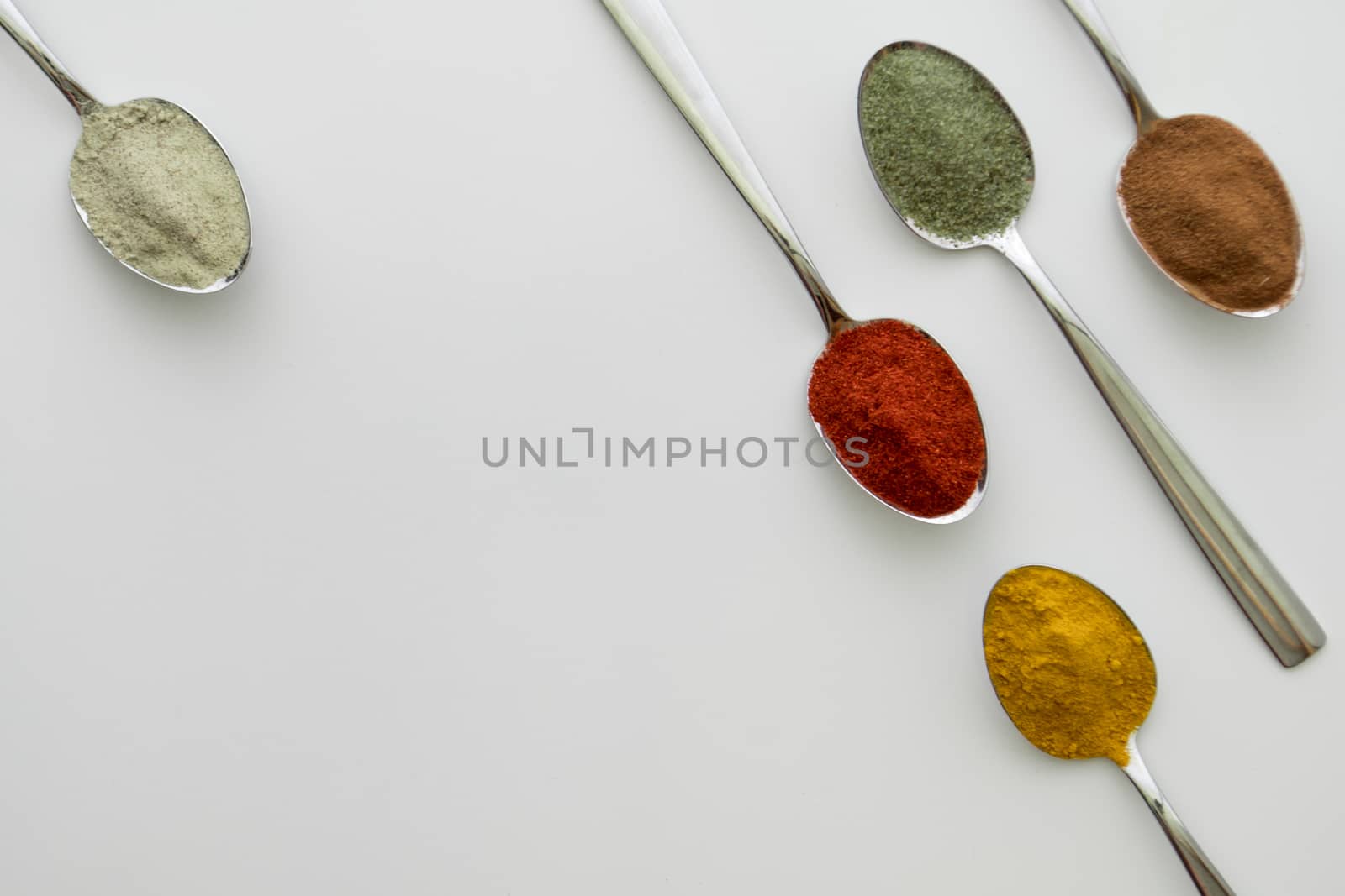 Various colorful spices arranged on spoons  with a white background