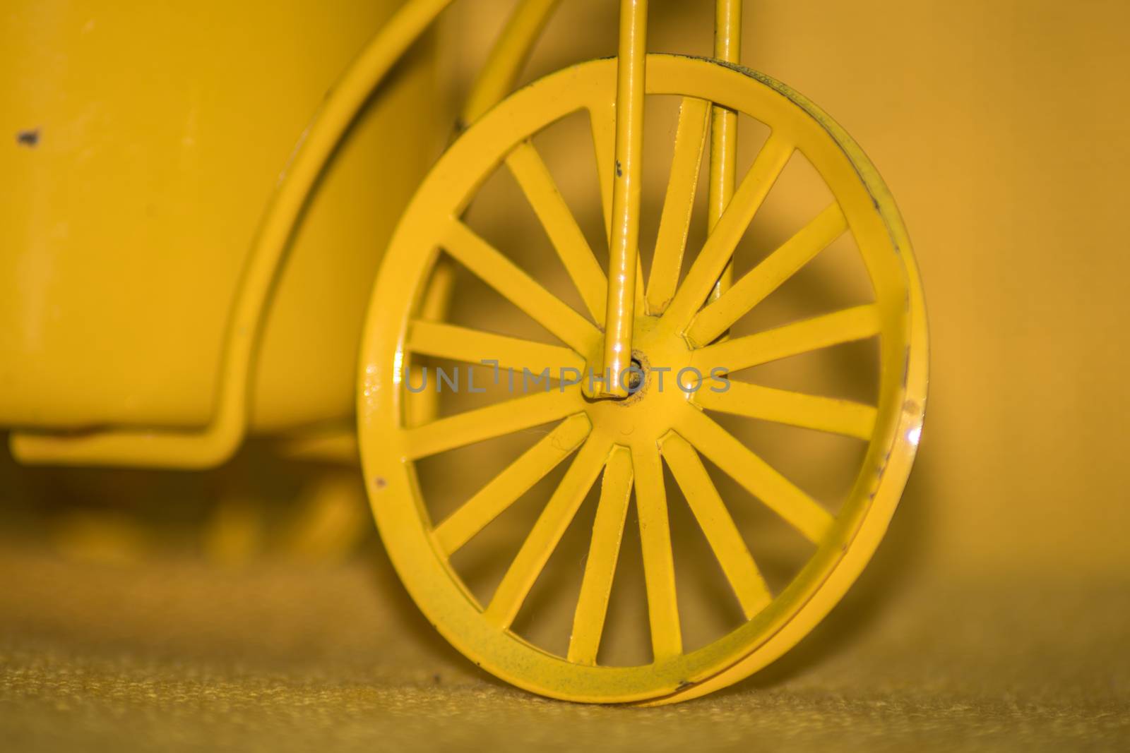 Closeup of a yellow toy wheel infront of a yellow background