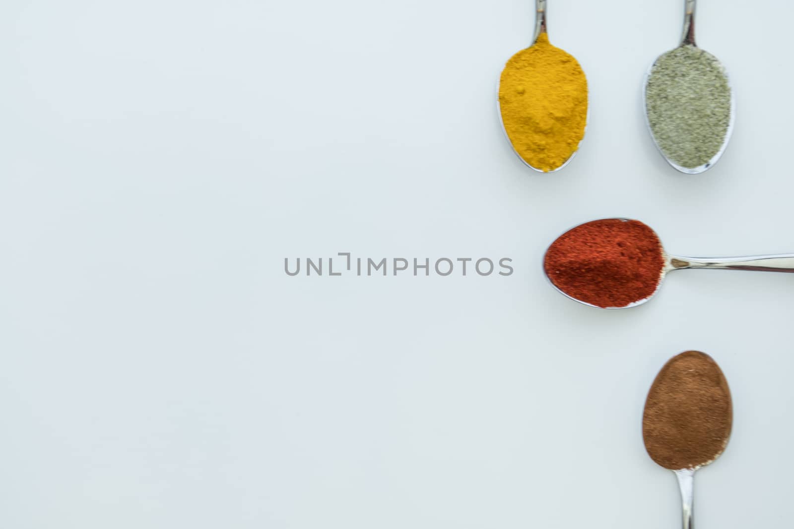 Various colorful spices arranged on spoons  with a white background