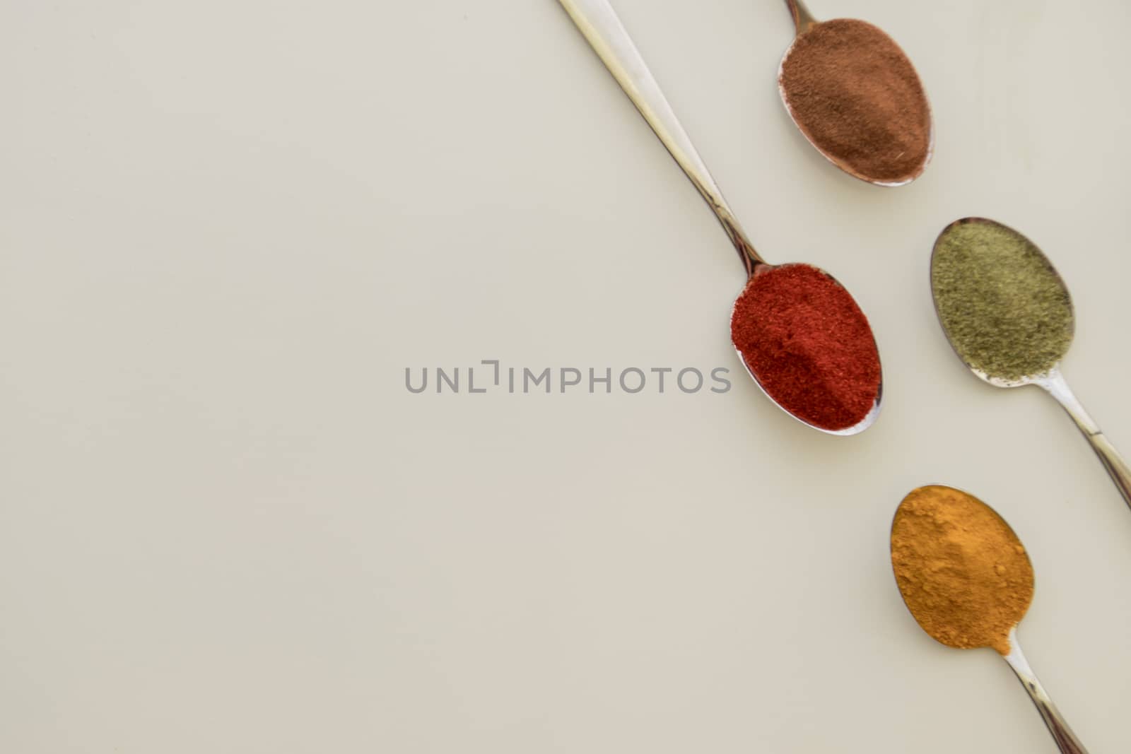 Various colorful spices arranged on spoons  with a white background