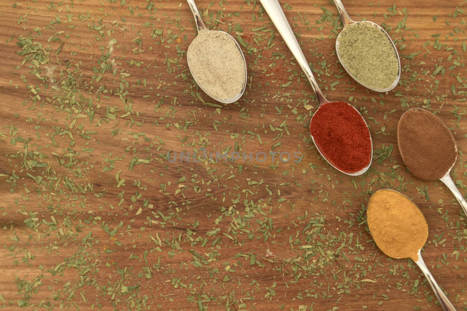 Various colorful spices arranged on spoons  with wooden background