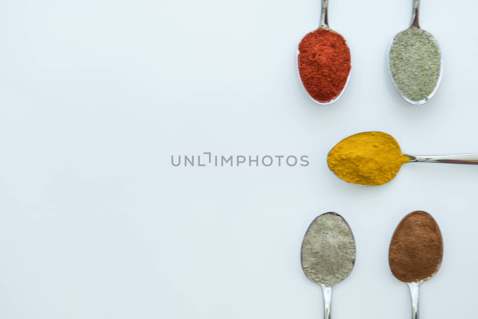 Various colorful spices arranged on spoons  with a white background