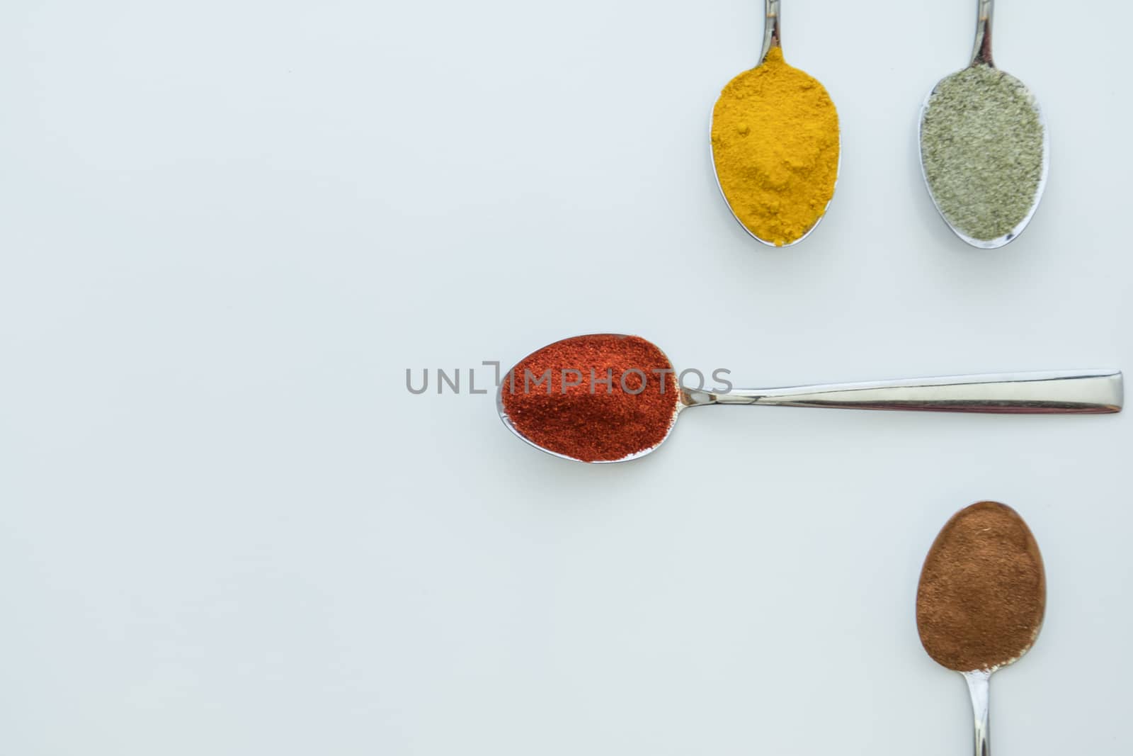 Various colorful spices arranged on spoons  with a white background