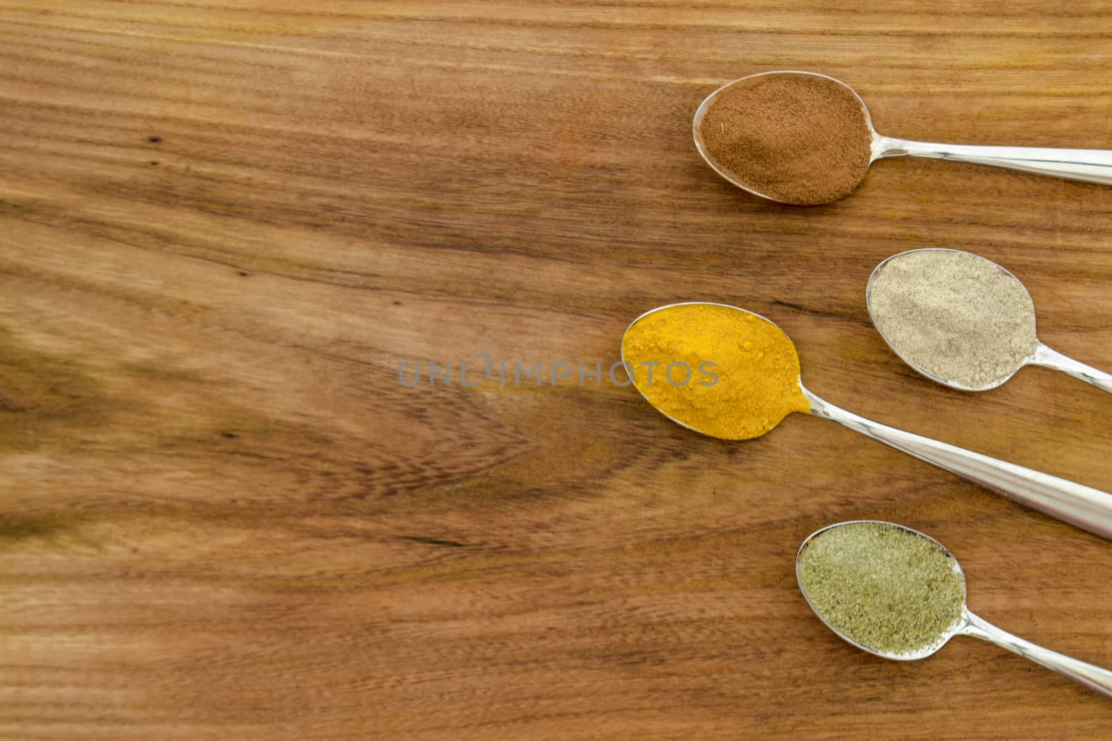 Various colorful spices arranged on spoons  with wooden background