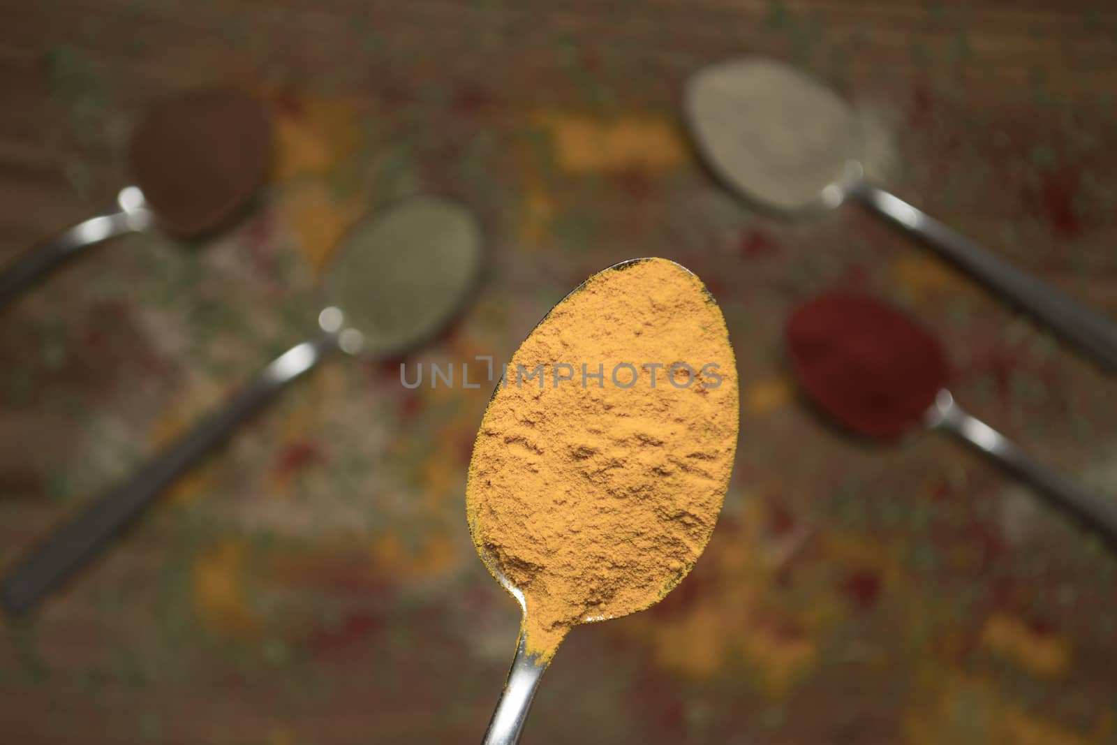 Closeup of yellow curry spice on a spoon with other spices in the background