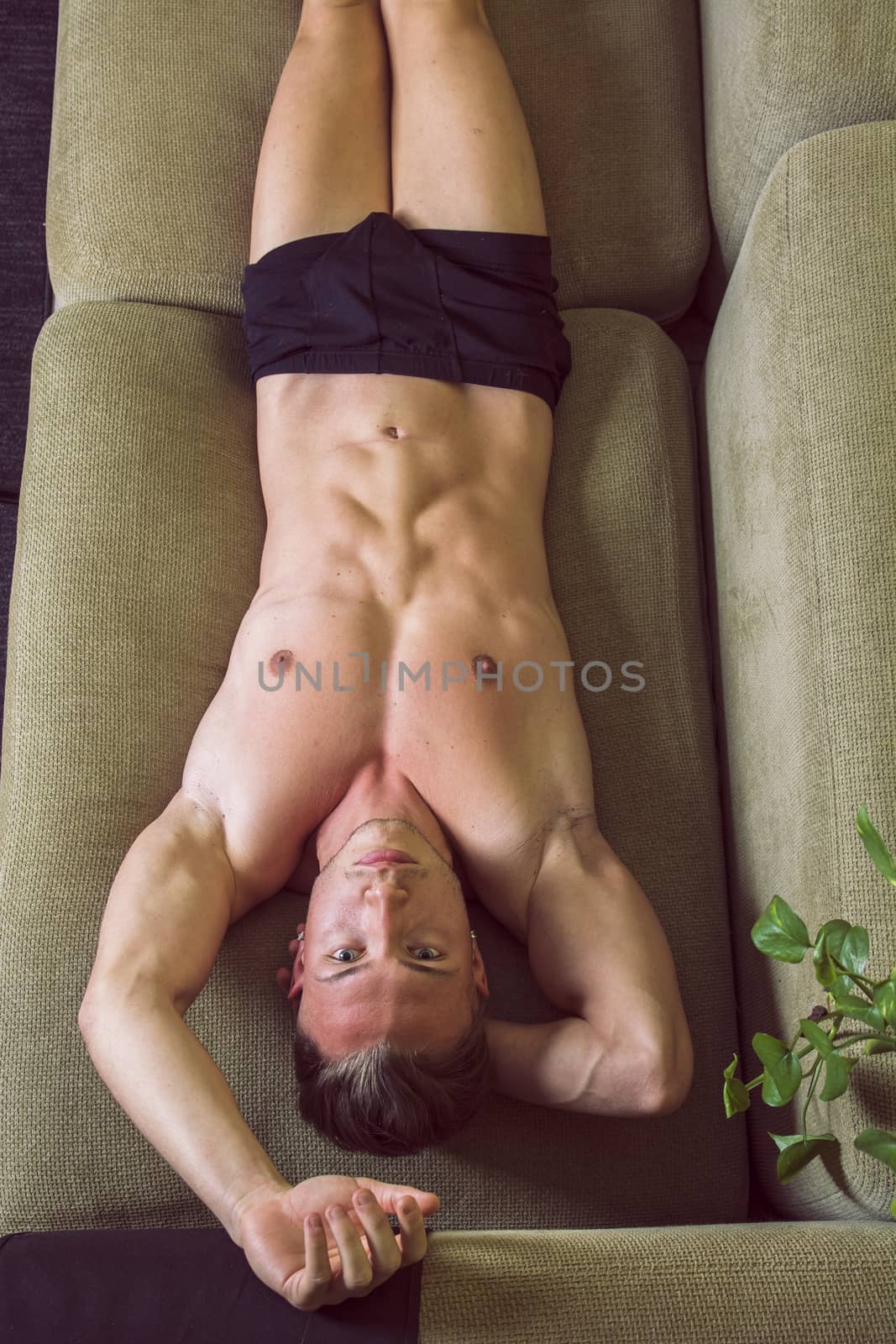 Shirtless, semi-naked fit young man resting on couch, seen from above