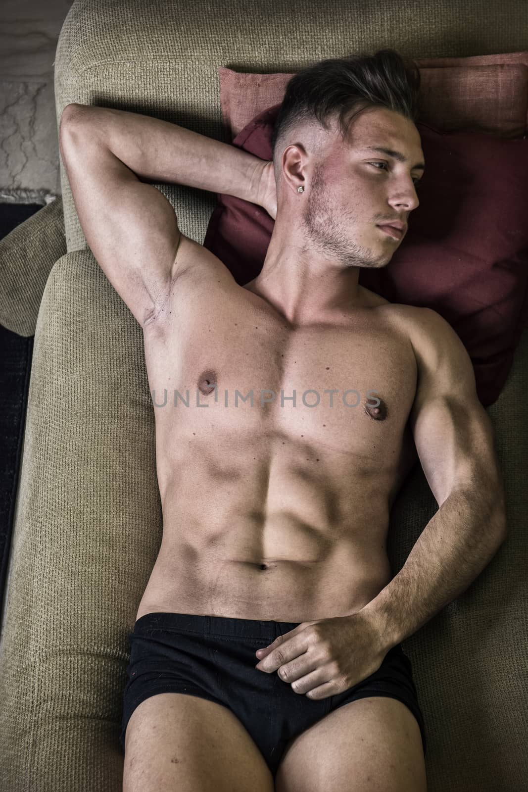 Shirtless, semi-naked fit young man resting on couch, seen from above