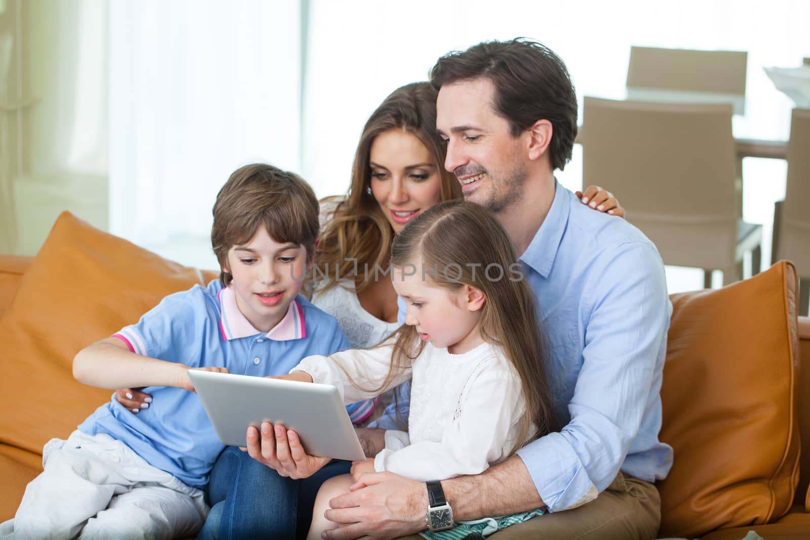 Portrait of happy family with two children sitting on sofa and using digital tablet pc