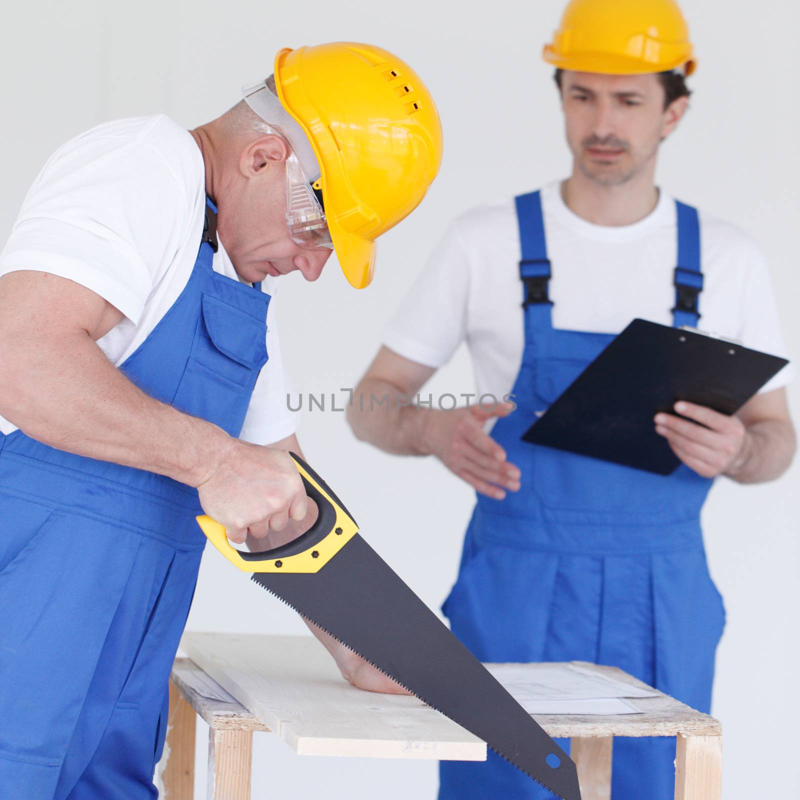 Worker works with handsaw, foreman on background