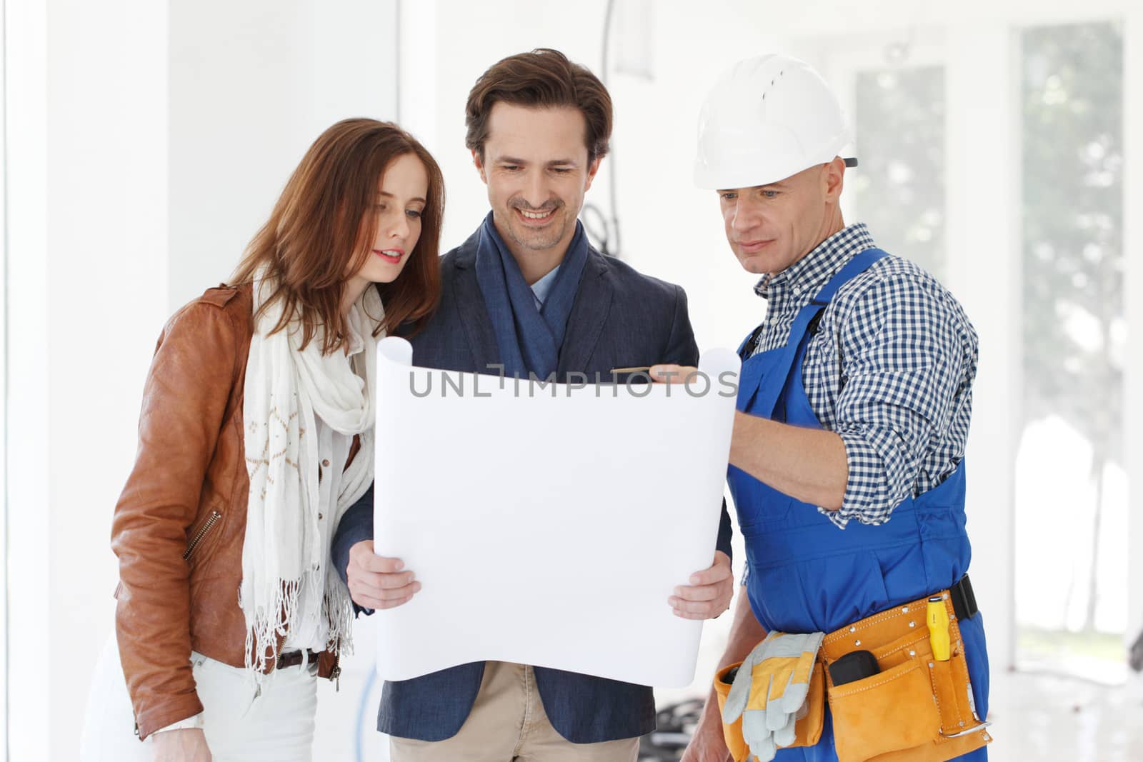 Worker shows house design plans to a young couple at construction site