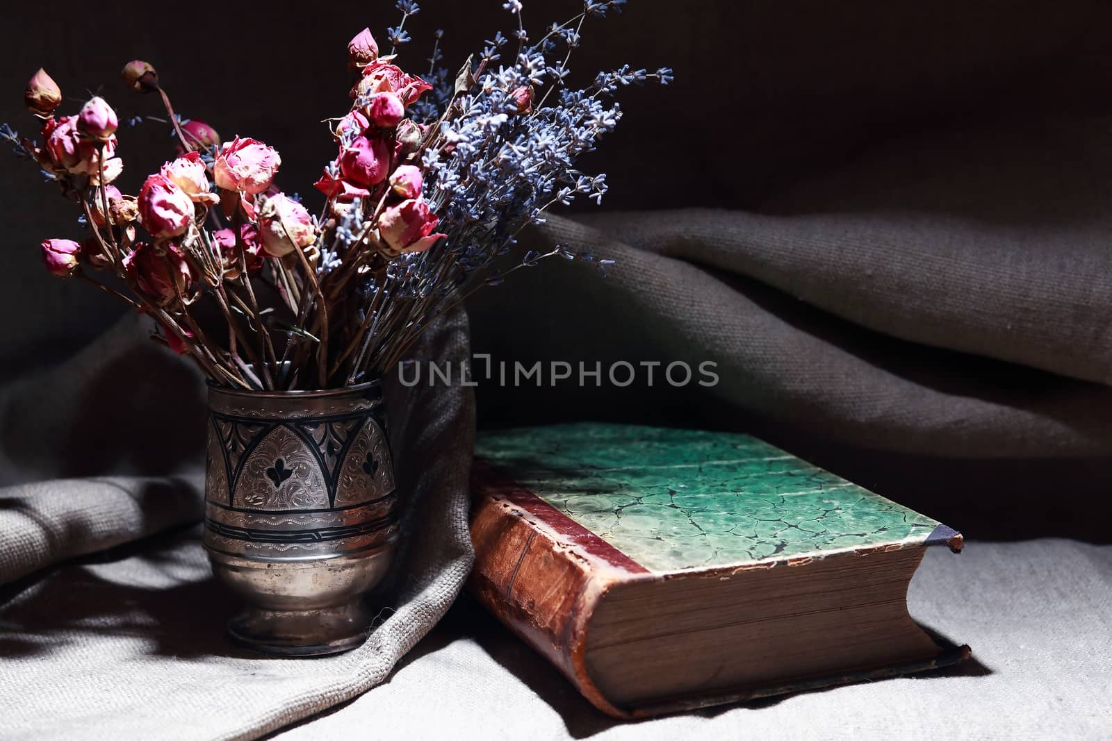 Vintage still life with bouquet of dried flowers in a silver vase near old book