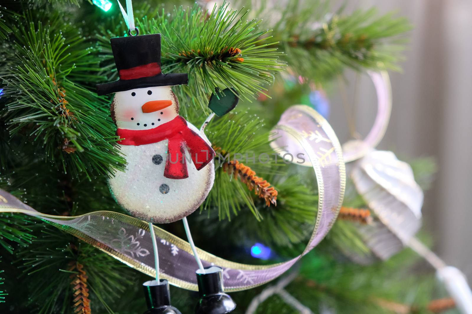 Toy funny iron snowman hanging on Christmas tree. New Year, holiday background with place for text. Pine decorated with ribbons and garlands. Front view. Horizontal.